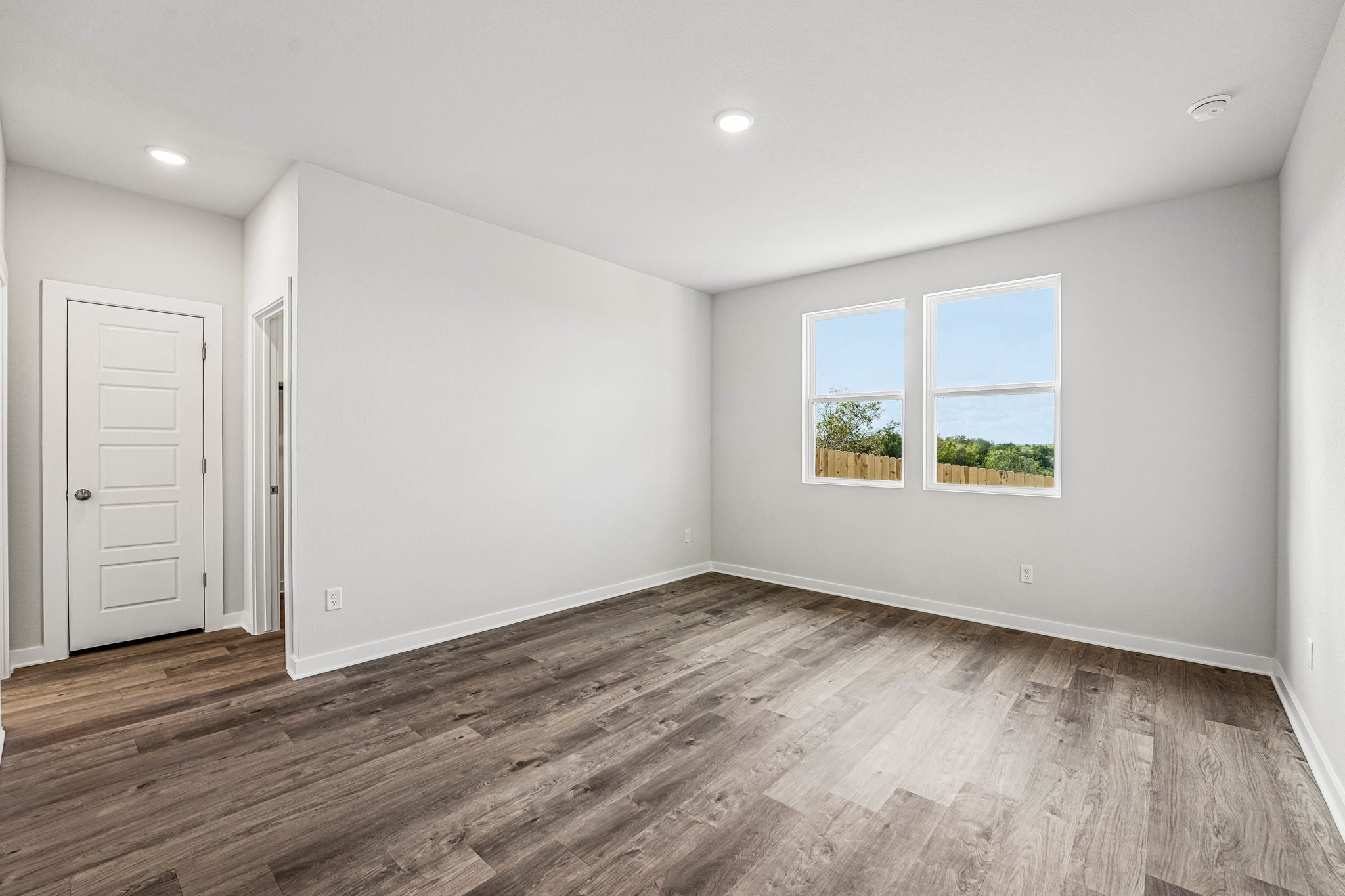 A room with a wood floor and a window with a tree outside.