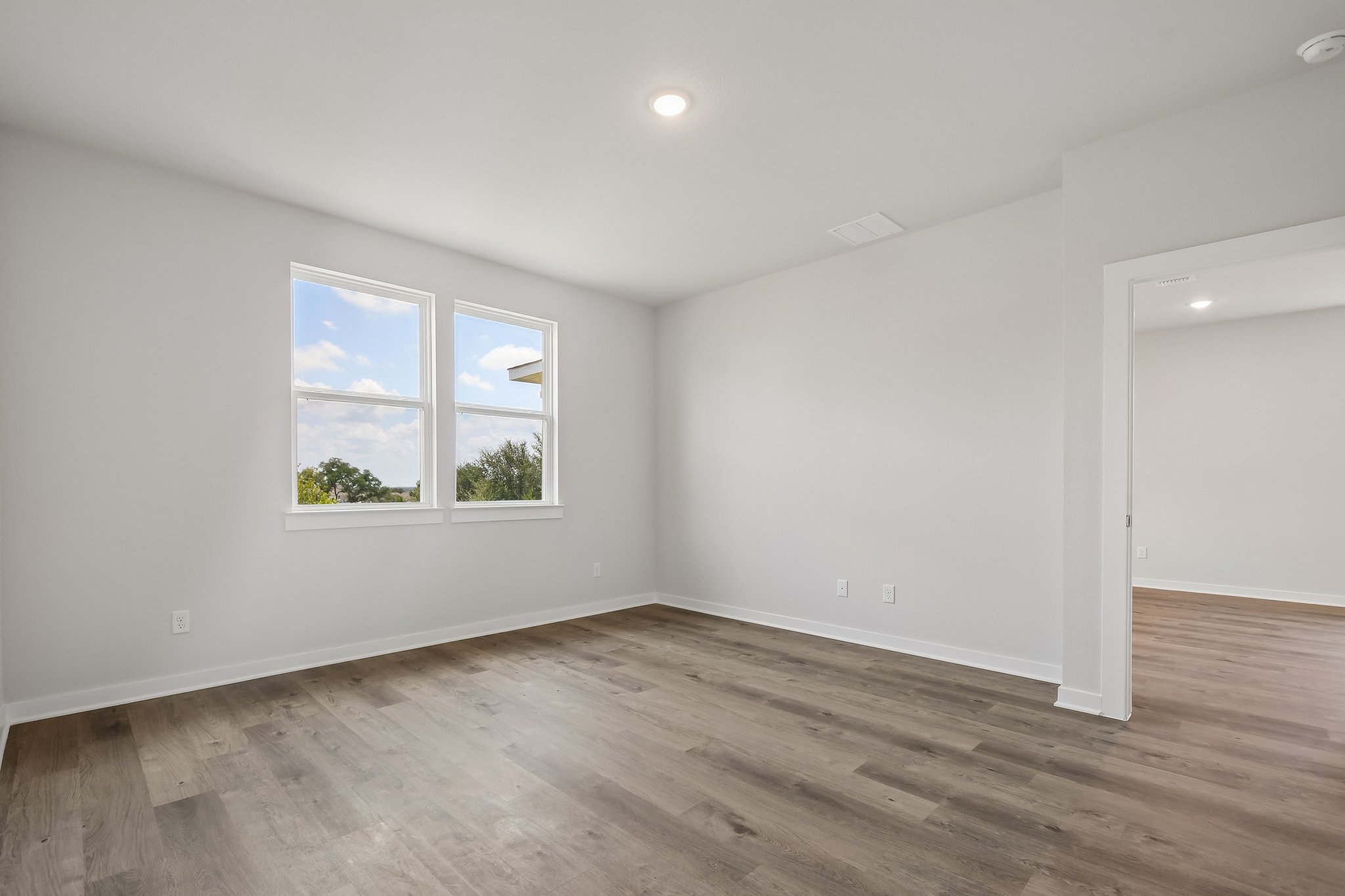 A room with a wood floor and a window with a view of trees.