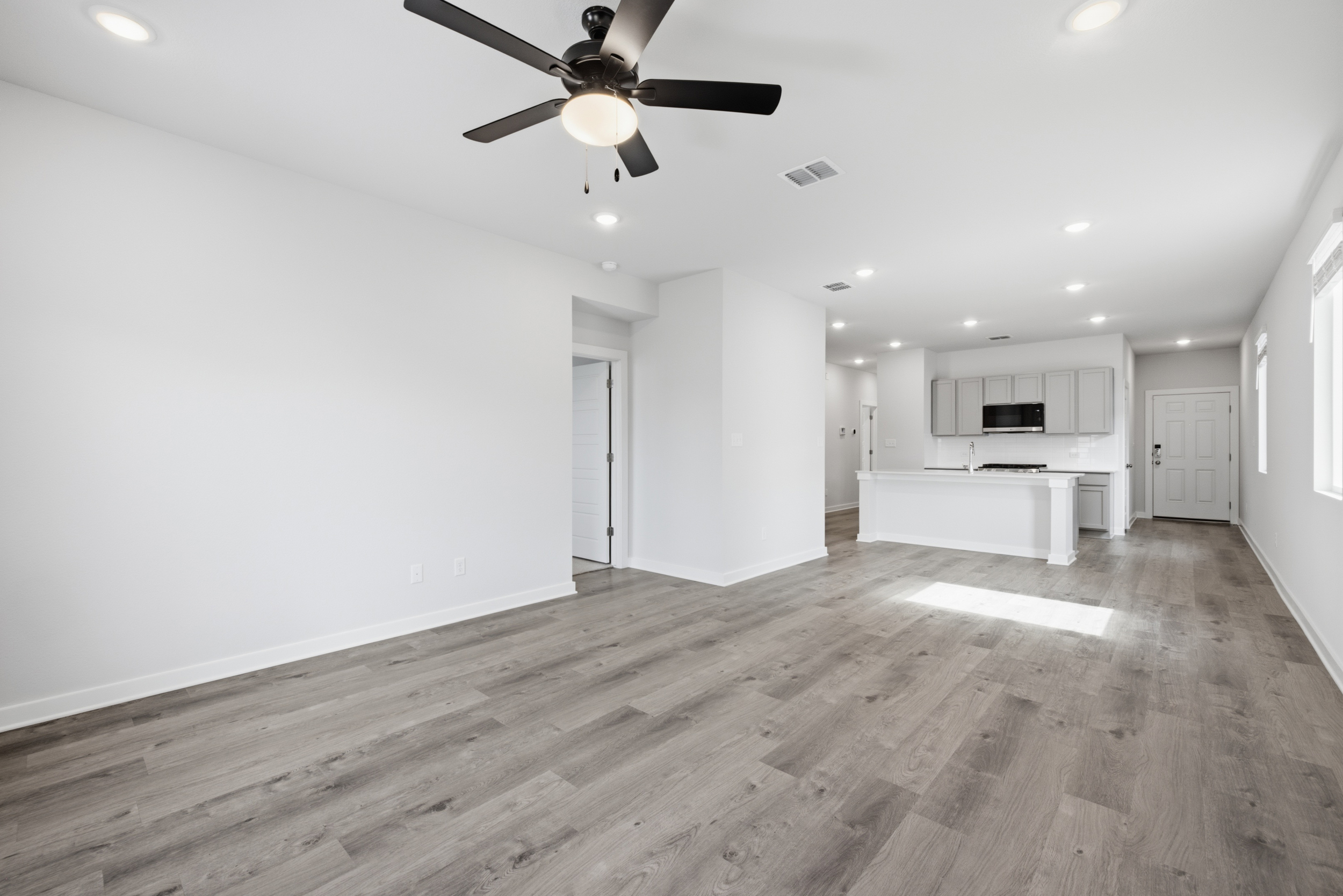 A large empty room with a wood floor and a ceiling fan.