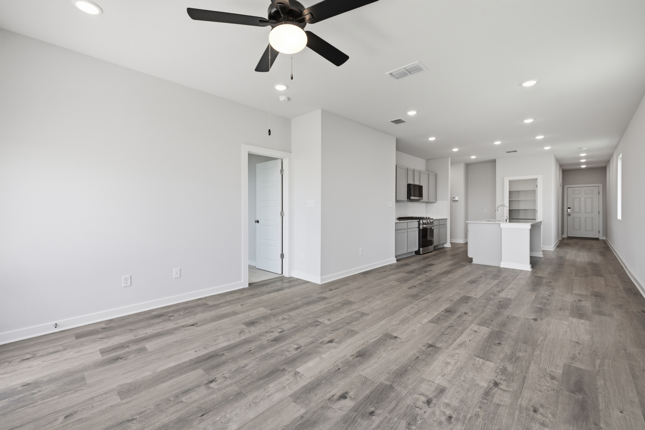 A large empty room with a ceiling fan and a wood floor.