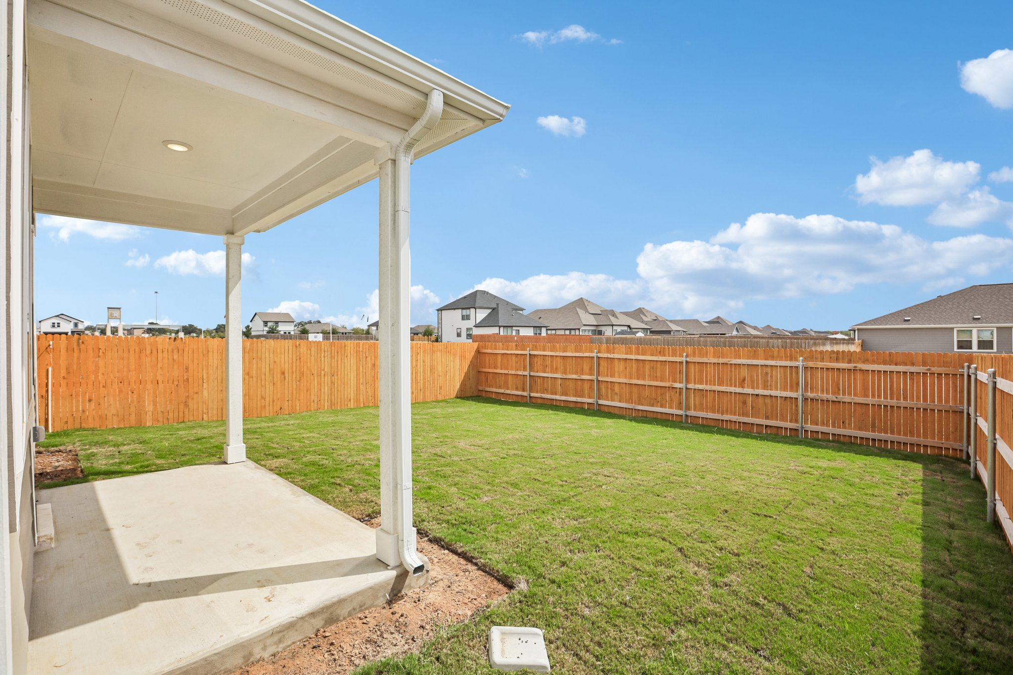 A fenced in yard with a covered area and a building in the background.