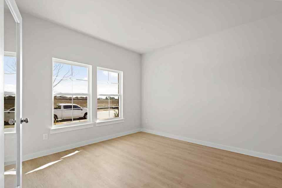 A room with a wood floor and a white wall with a car parked in it.