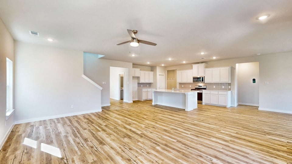 A large empty room with a wood floor and a ceiling fan.