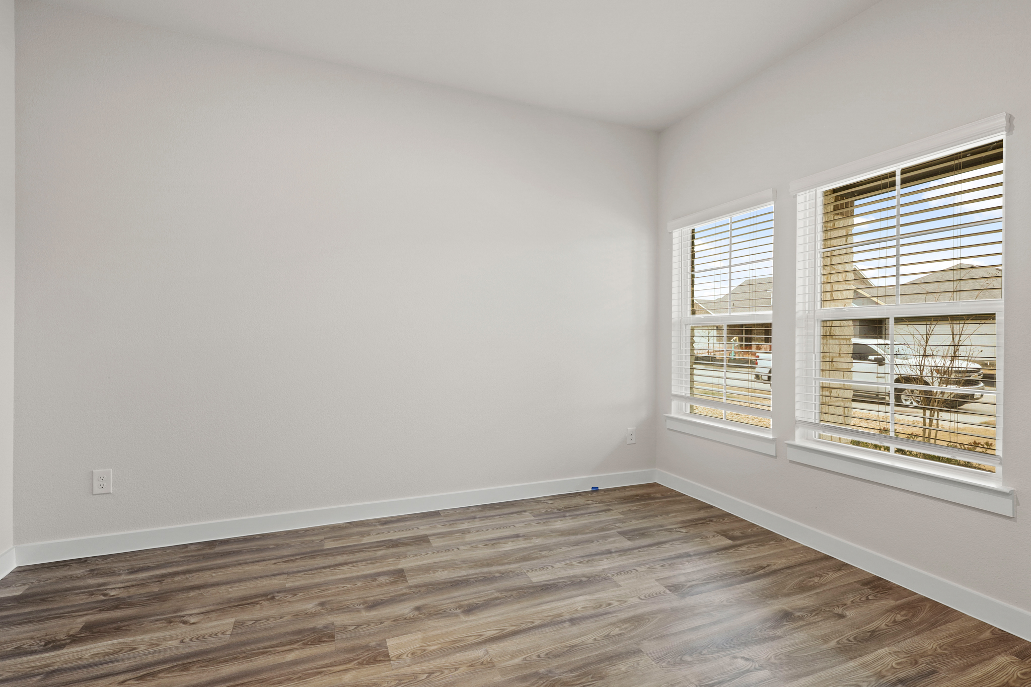 A room with a wood floor and a window with blinds.