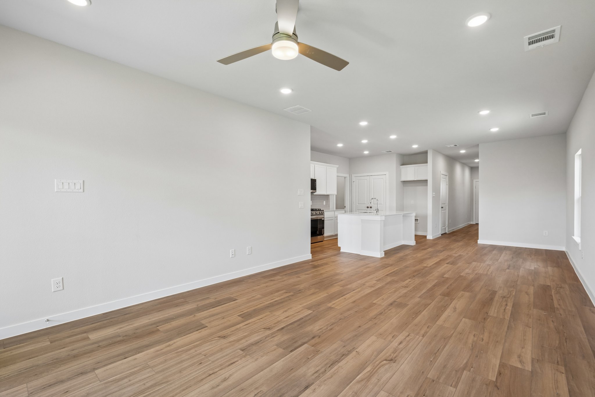 A large empty room with a ceiling fan and a wood floor.