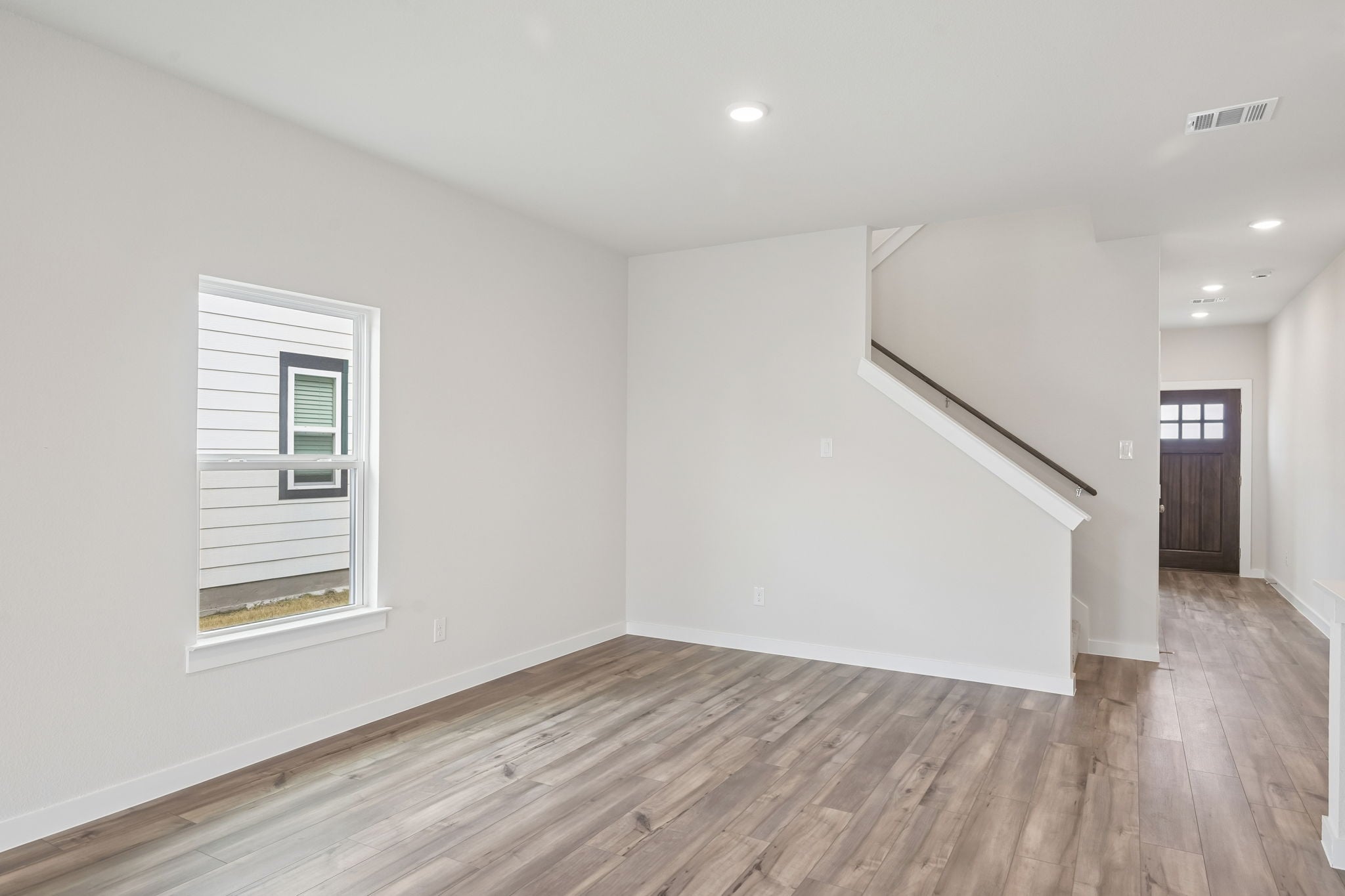 A room with a wood floor and a white wall with a window.