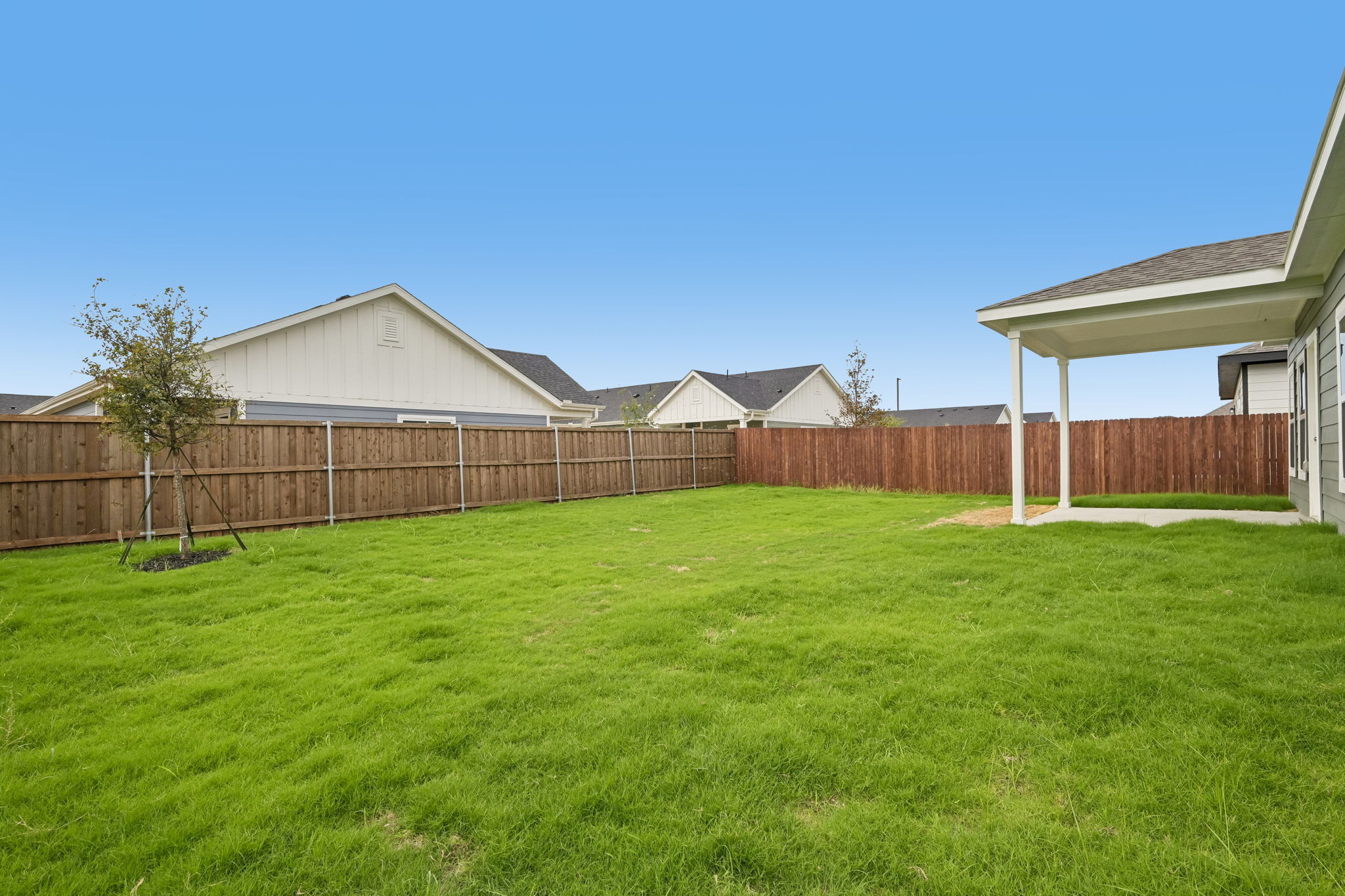 A fenced in yard with a tree and a house in the background.