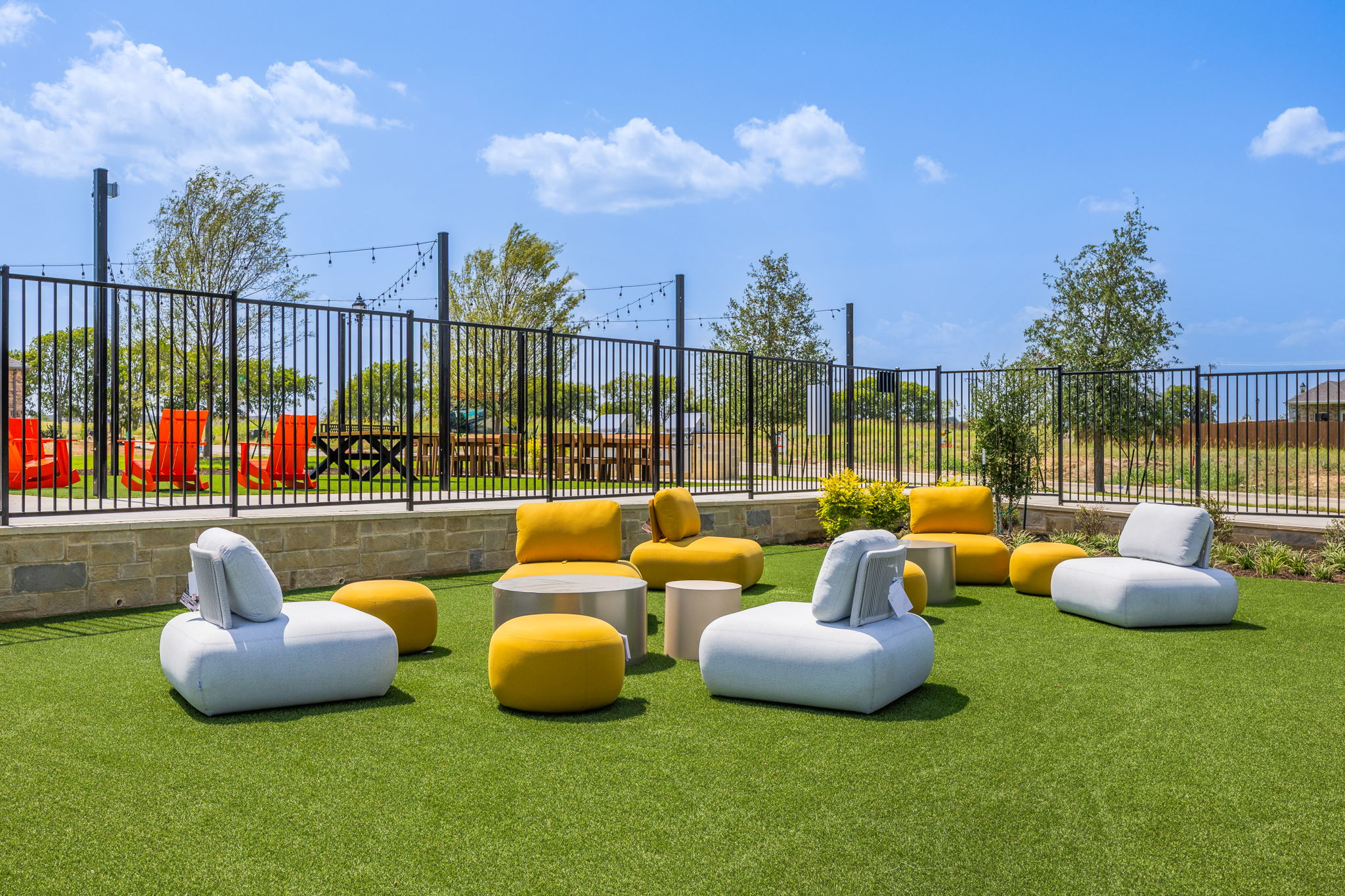 A group of white chairs in a grassy area with a fence and trees in the background.
