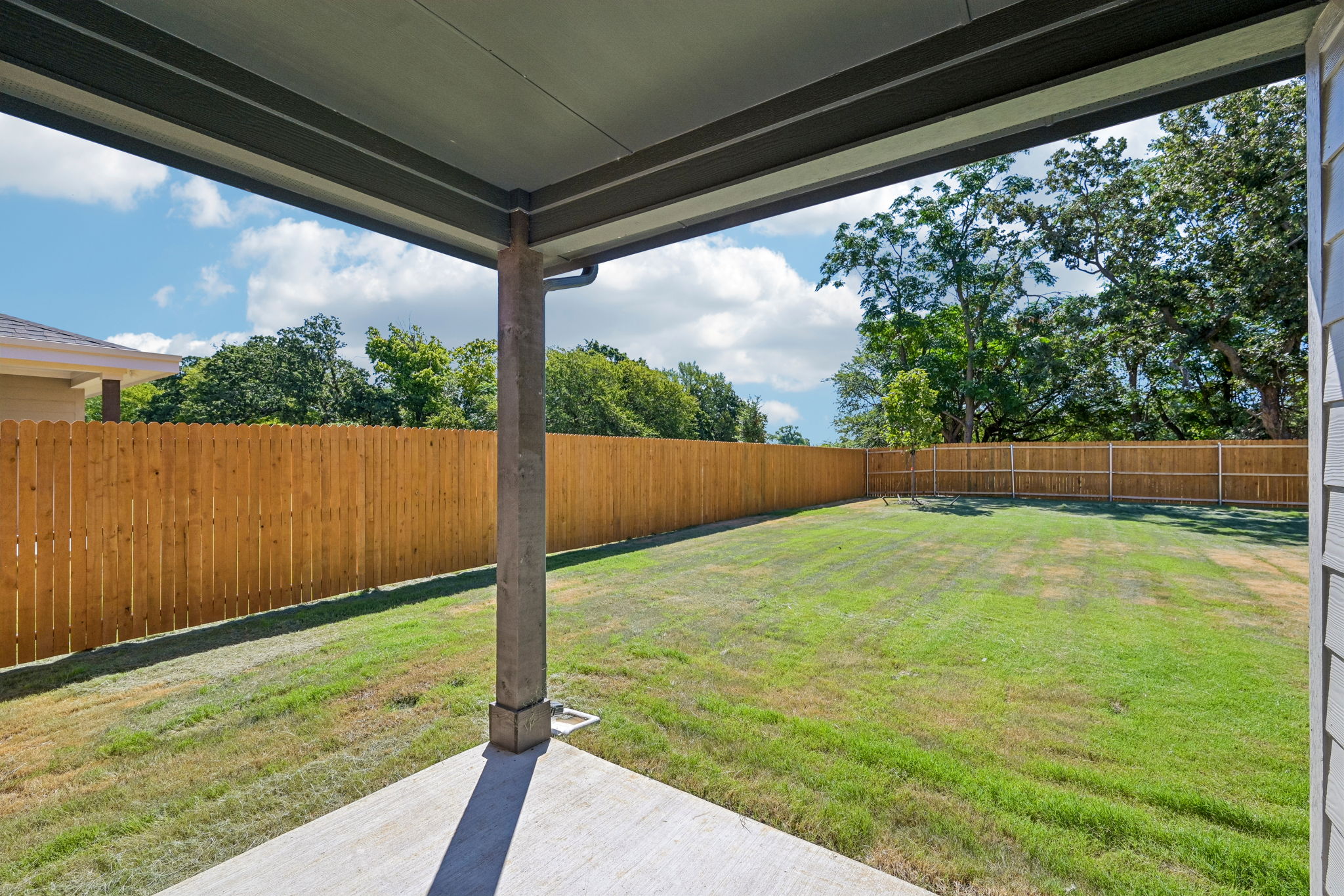 A fenced in yard with a wood gate and trees in the background.