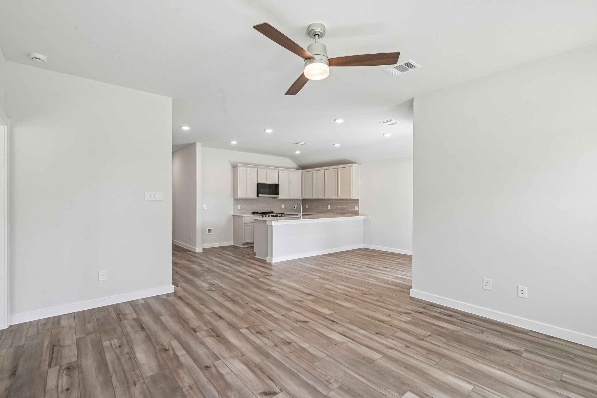 A large empty room with a wood floor and a ceiling fan.