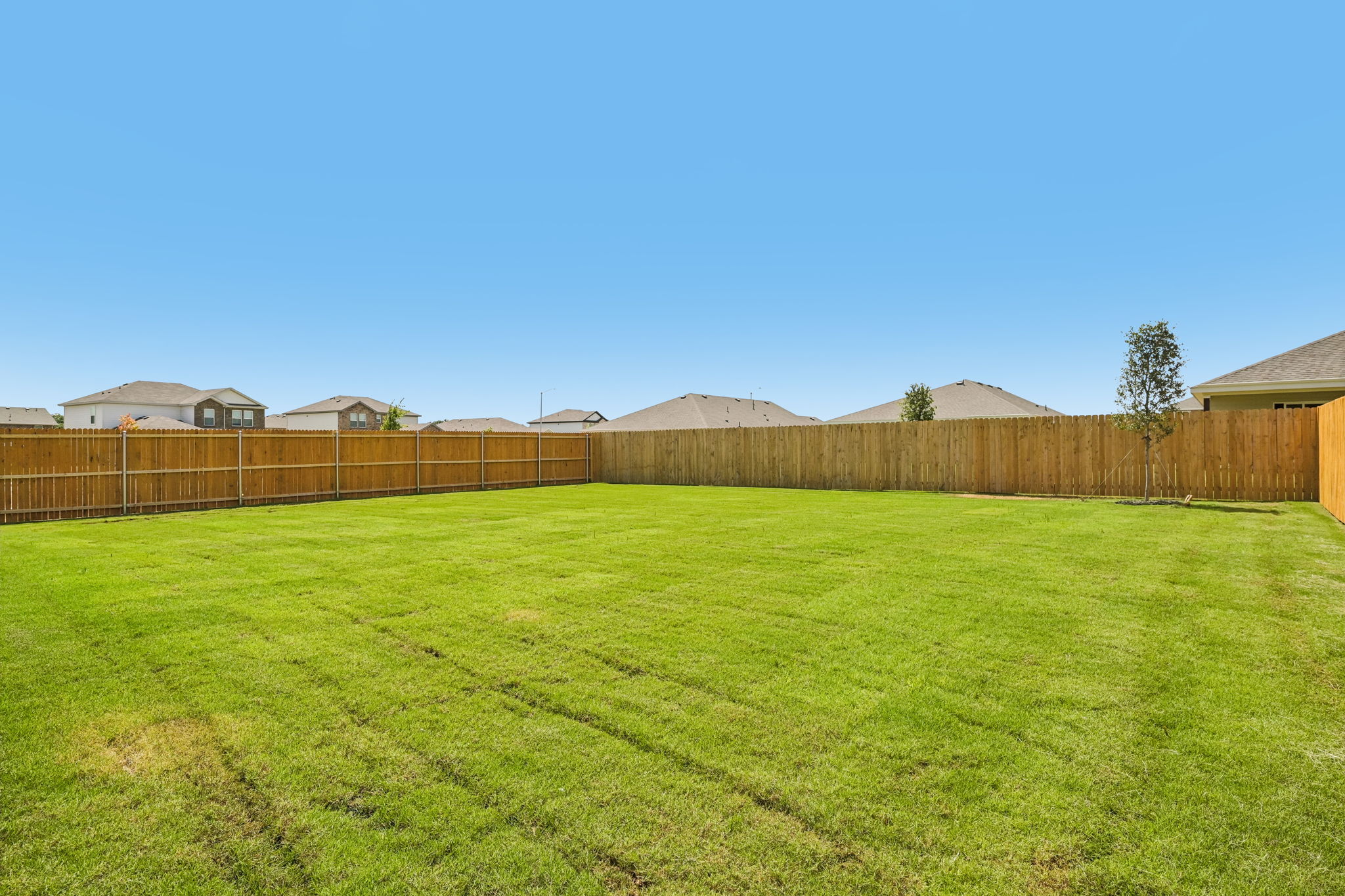 A fenced in yard with a field and houses in the background.