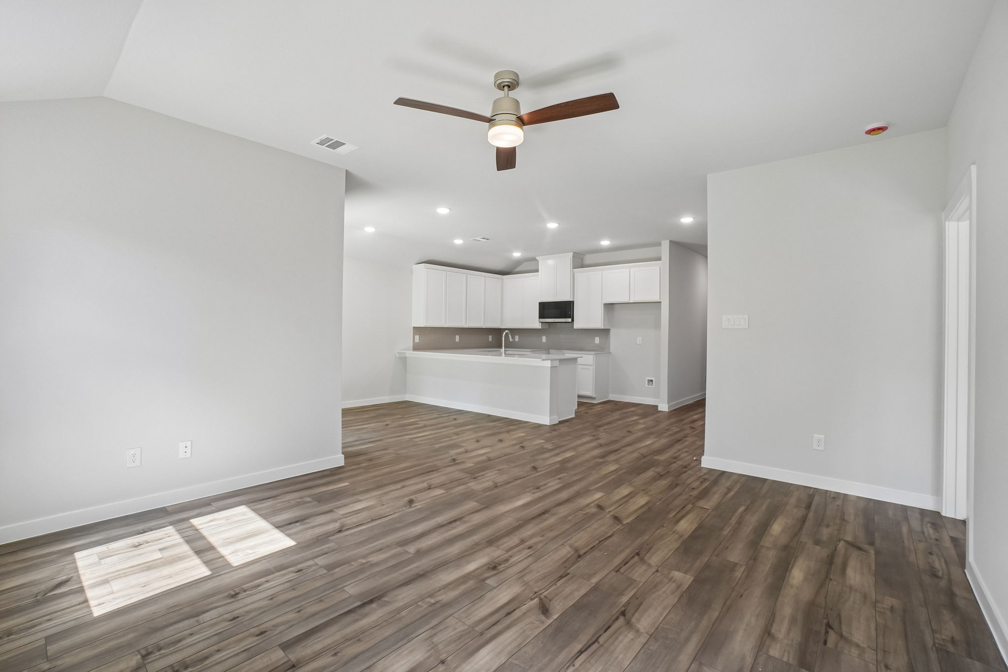 A large empty room with a wood floor and a ceiling fan.