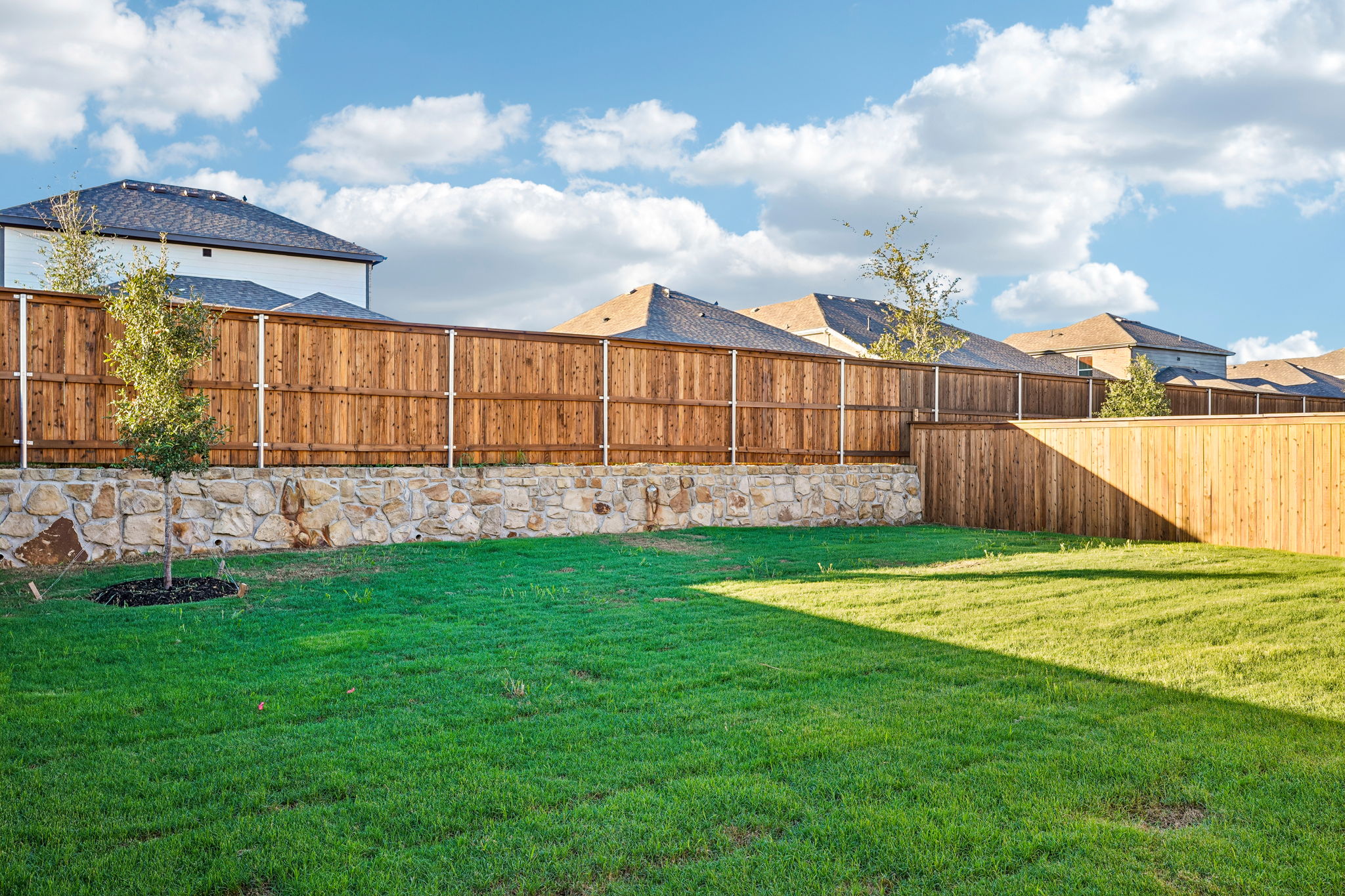 A fenced in yard with a stone wall and a building in the background.