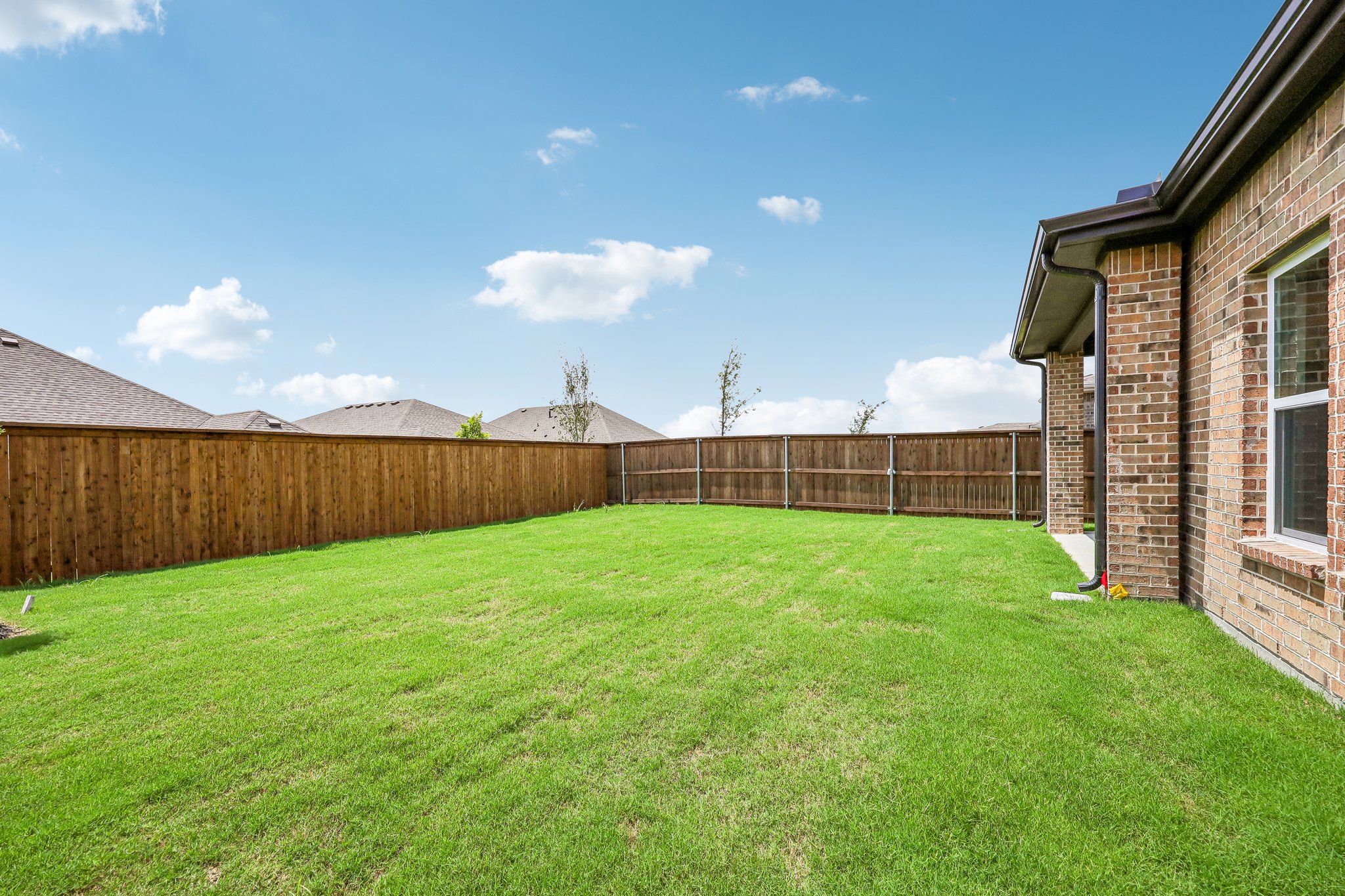 A grassy yard with a fence and a house in the background.