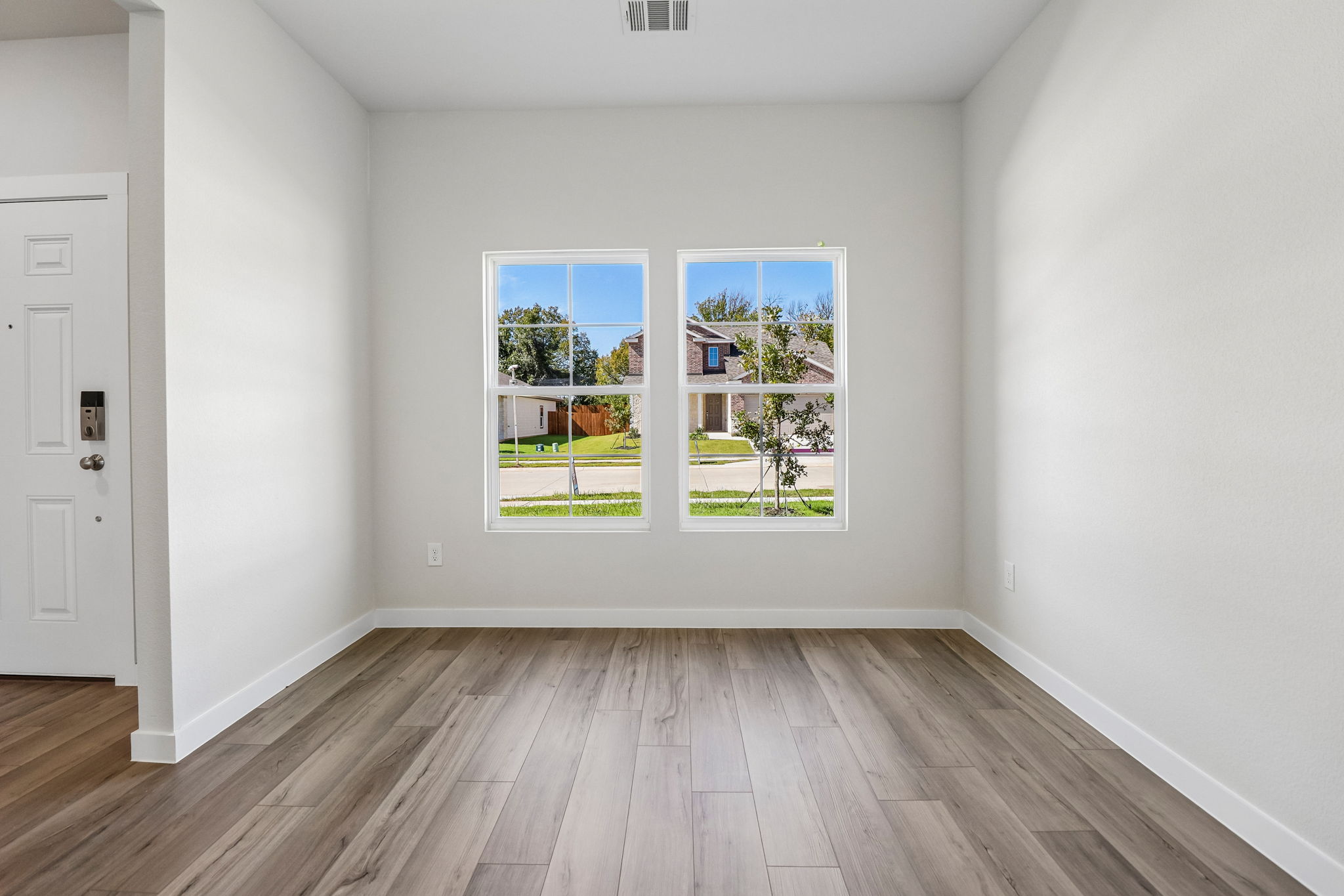 A room with a wood floor and a window with a view of a tree and a house.