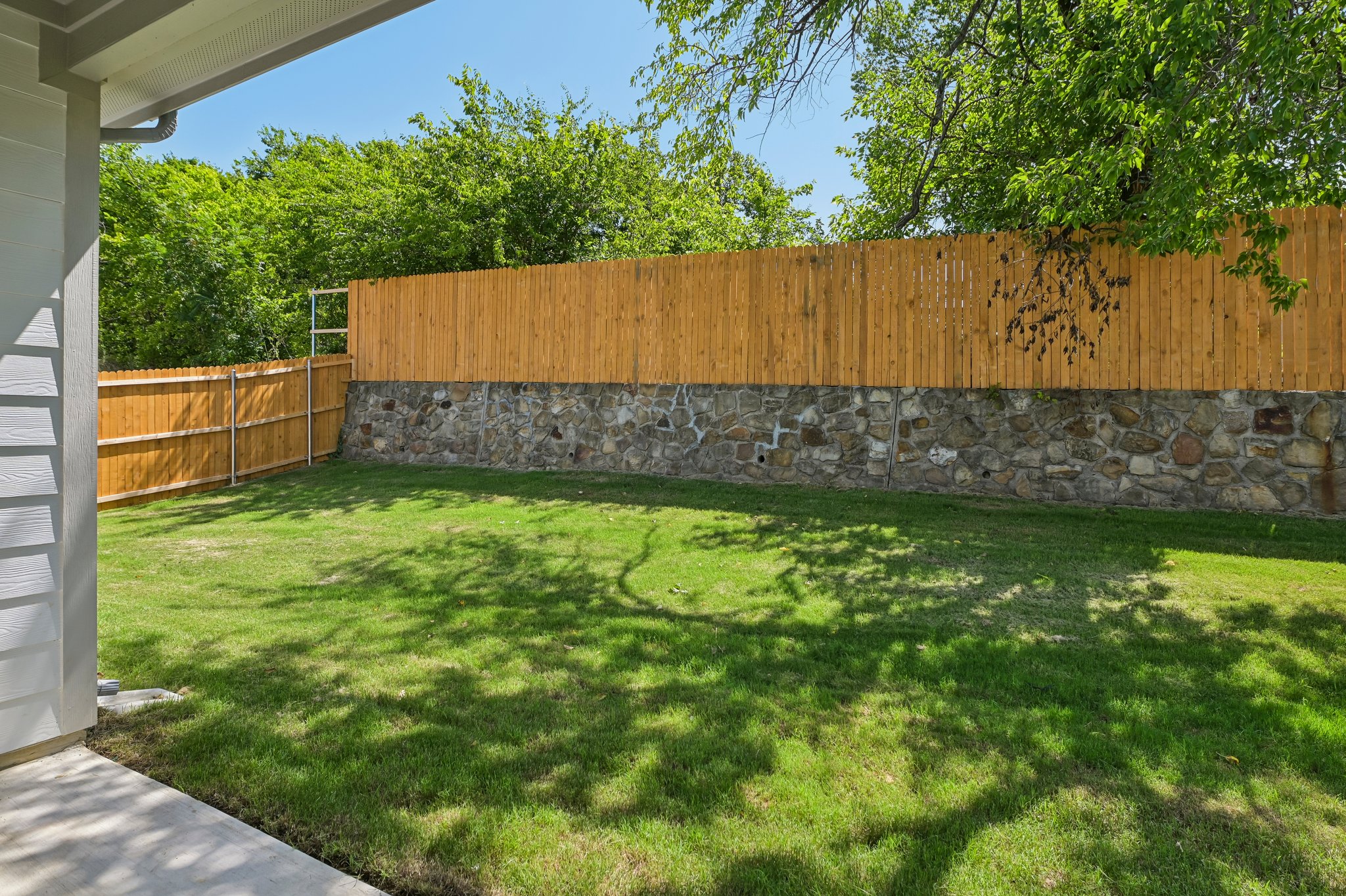 A fenced yard with a stone wall and grass.
