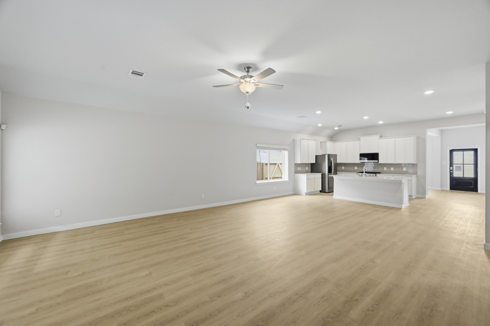 A large empty room with a ceiling fan and a wood floor.