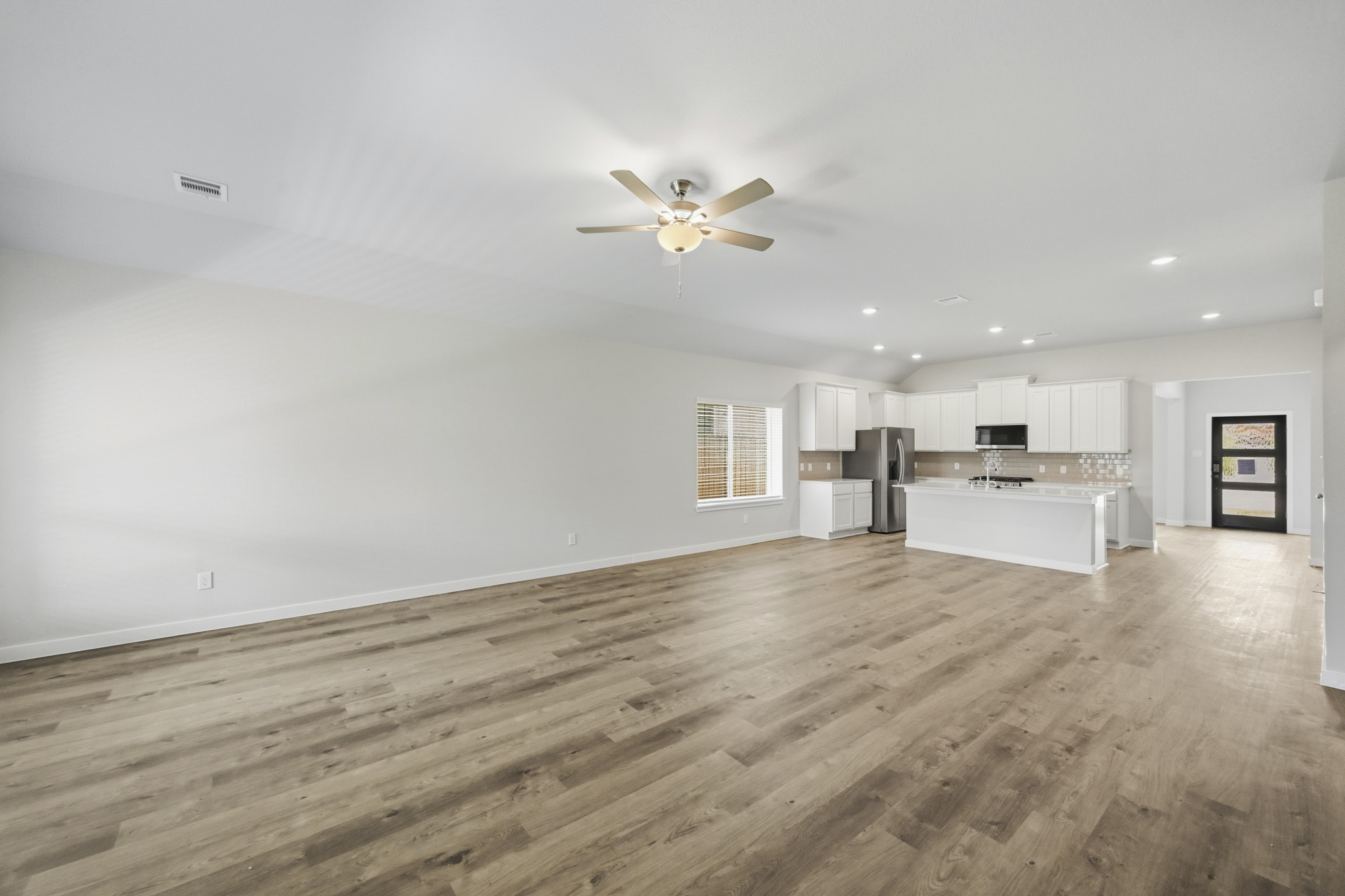 A large empty room with a ceiling fan and a wood floor.