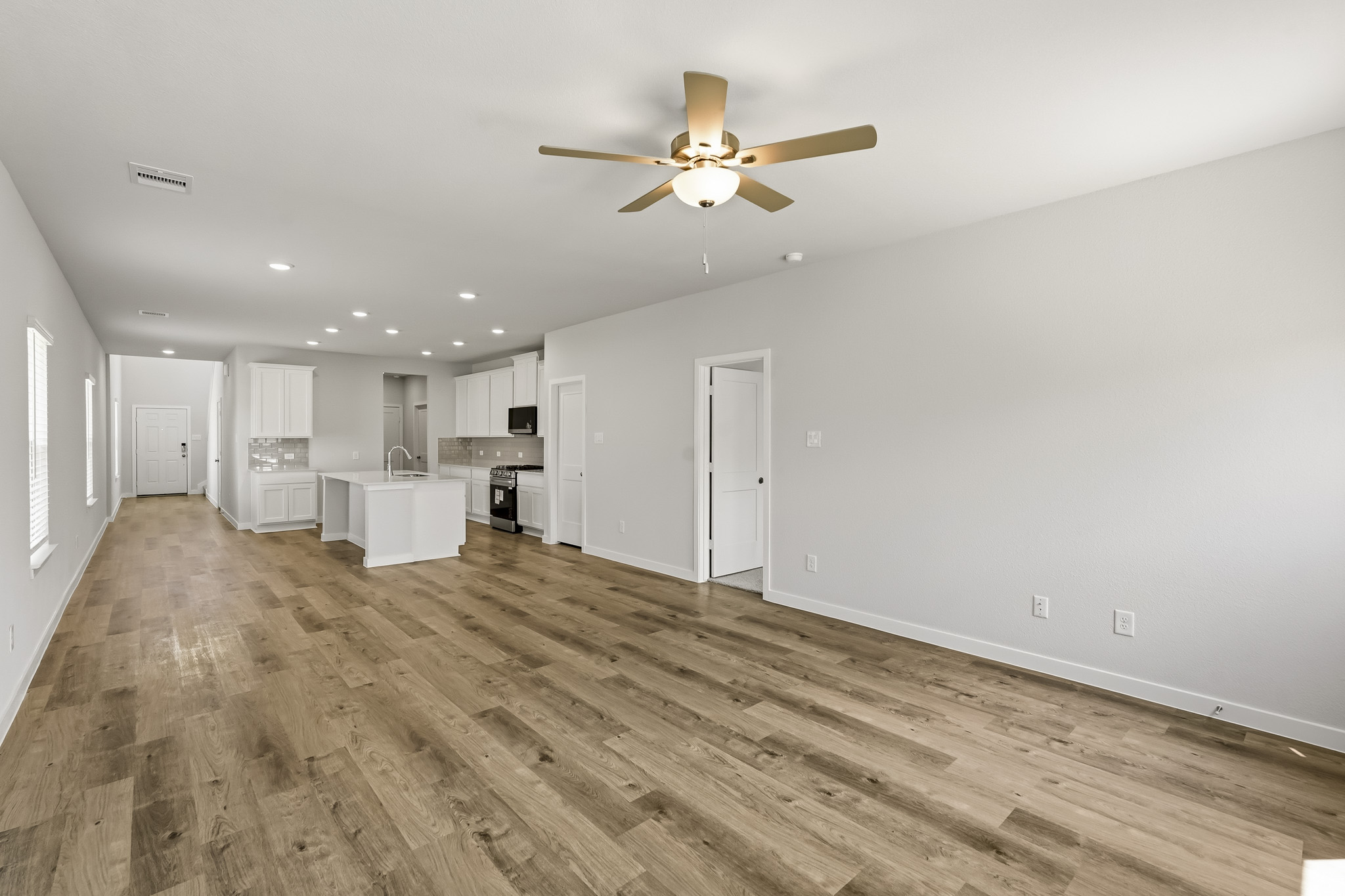 A large empty room with a ceiling fan and a wood floor.