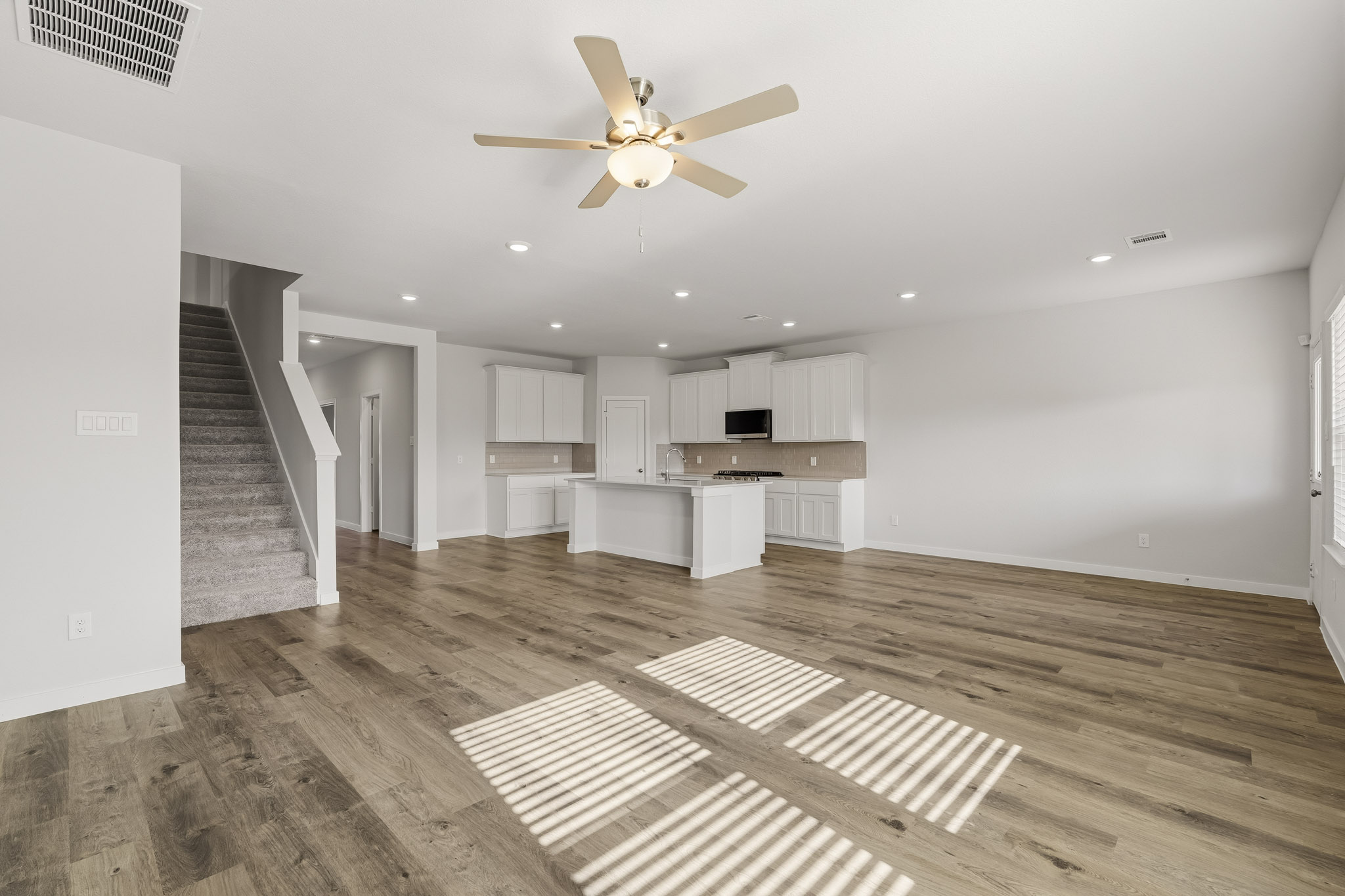 A large empty room with a wood floor and a ceiling fan.