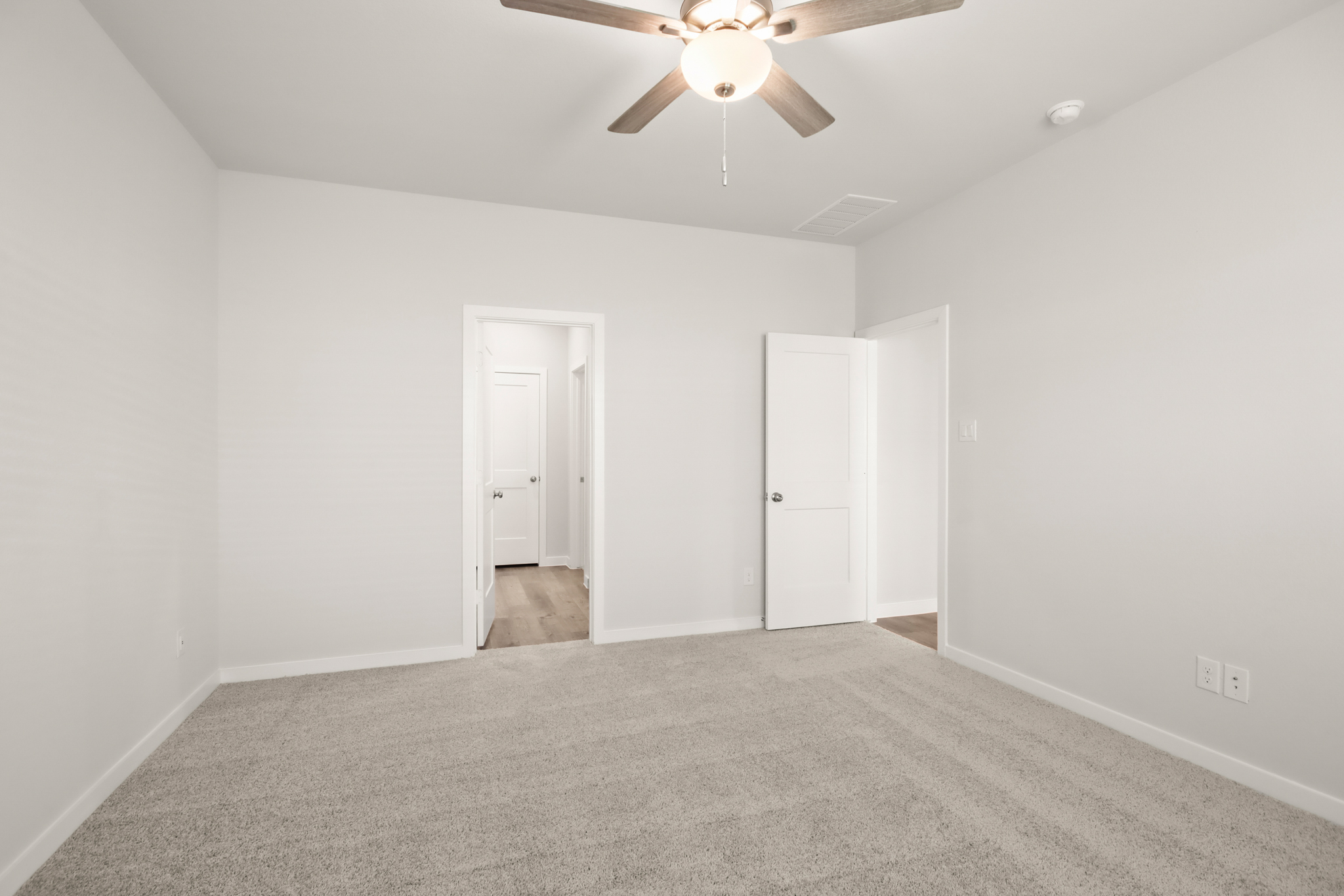 A room with a ceiling fan and white walls.