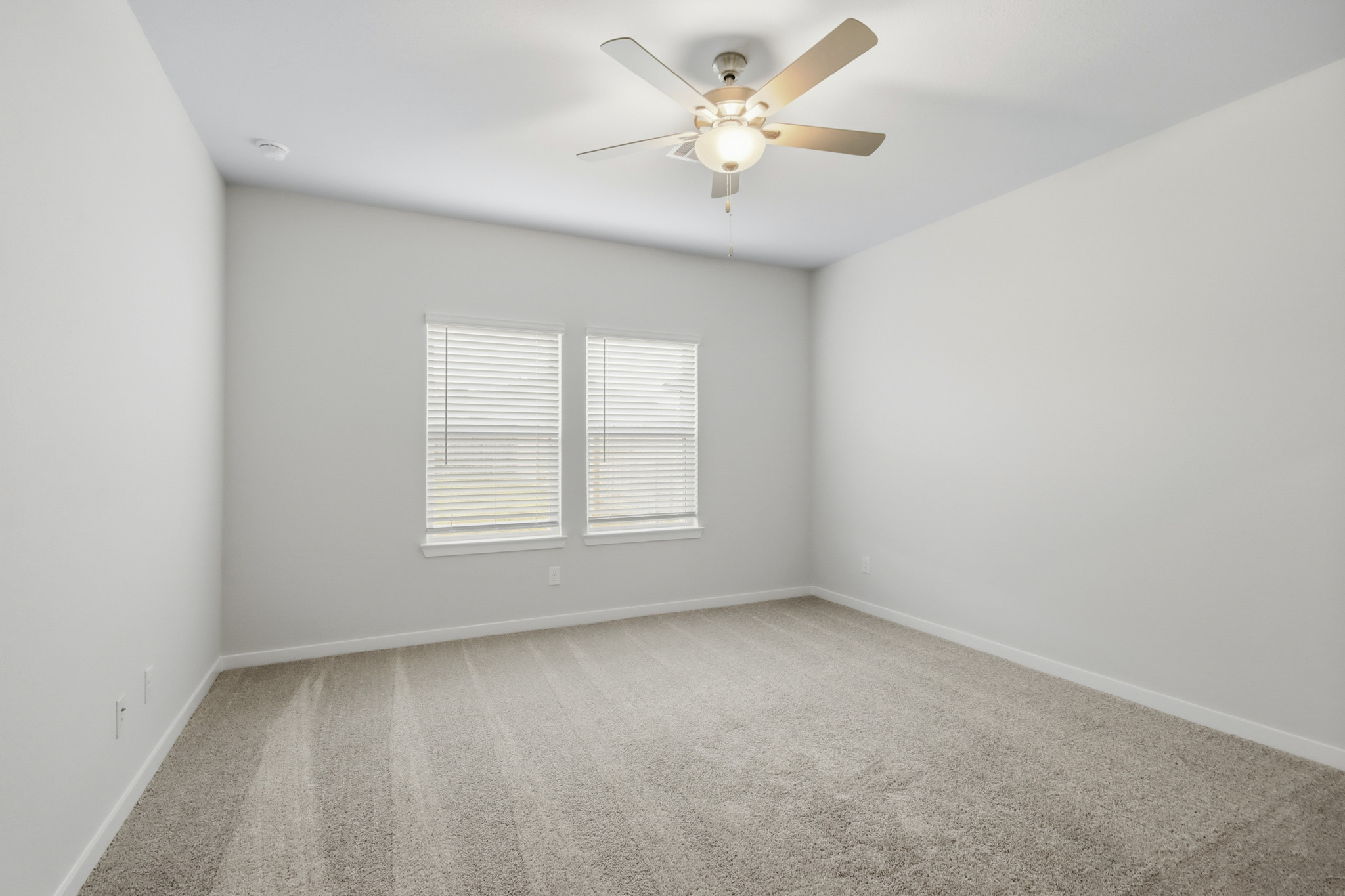 A room with a ceiling fan and a carpet.