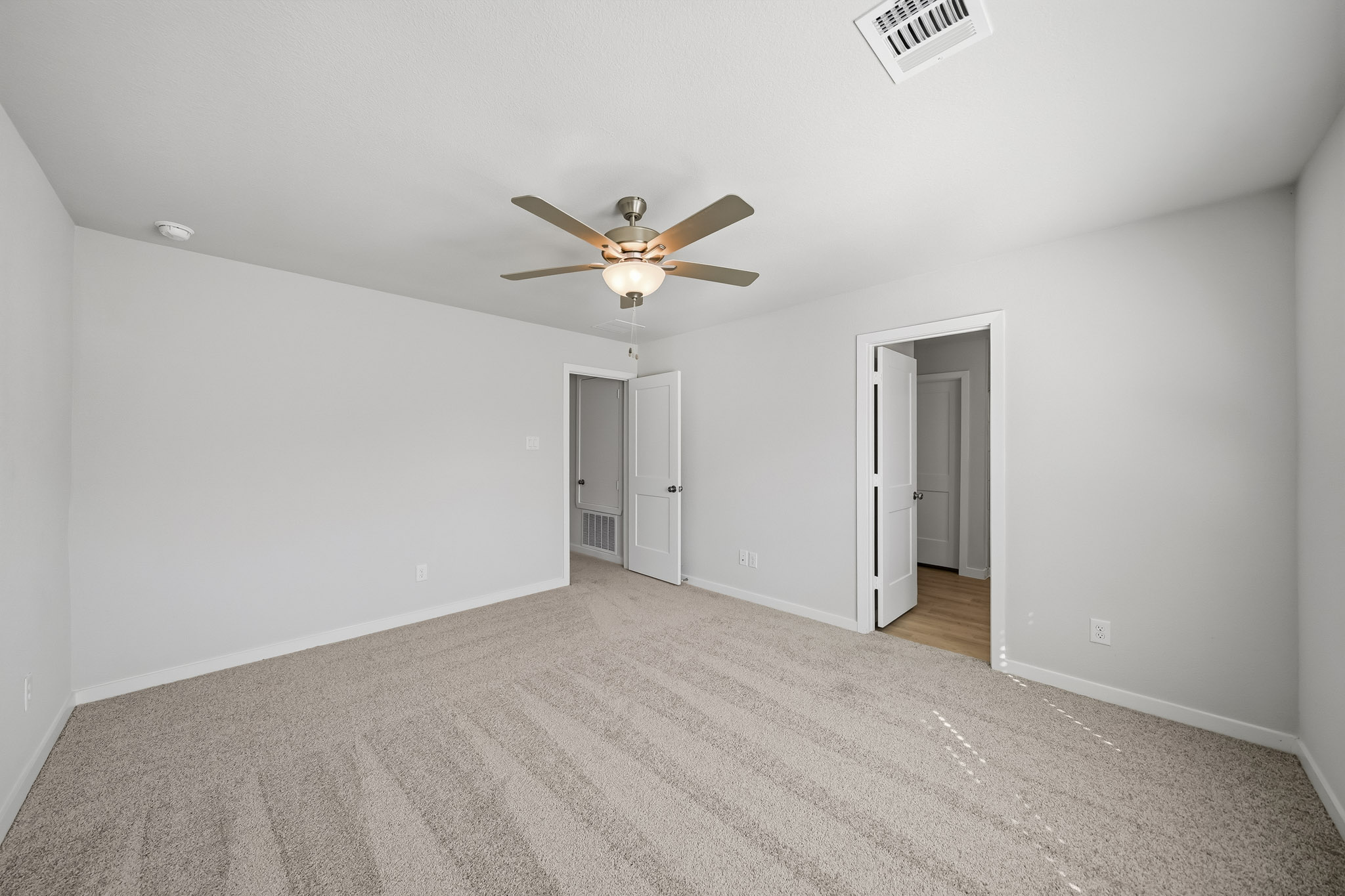 A room with a ceiling fan and a carpet.