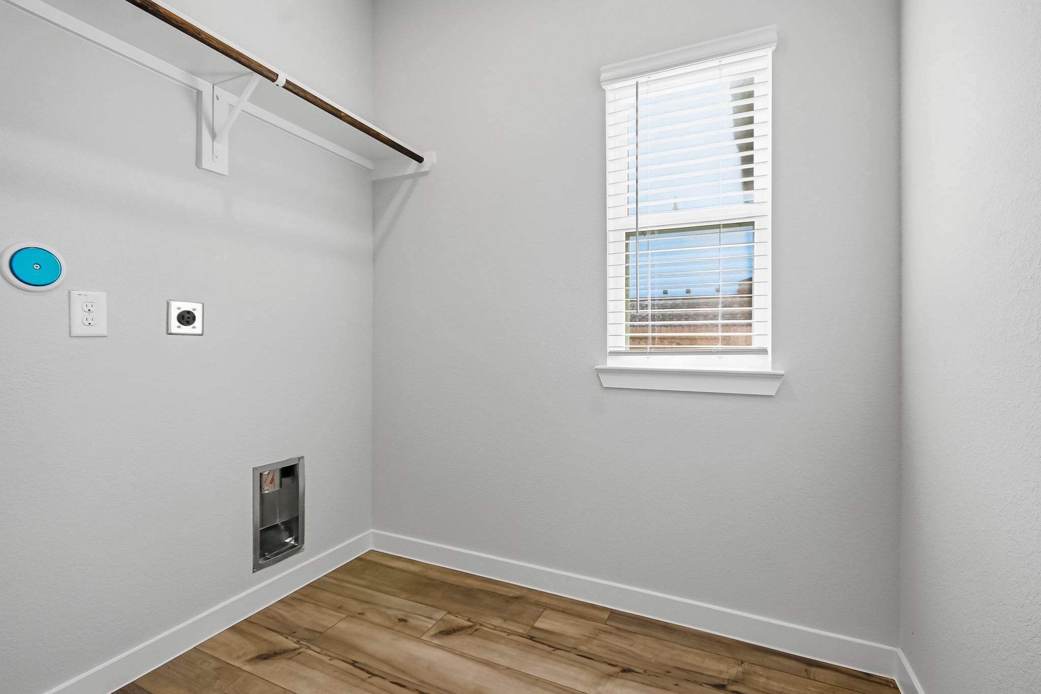 A room with a wood floor and a window with a vent.