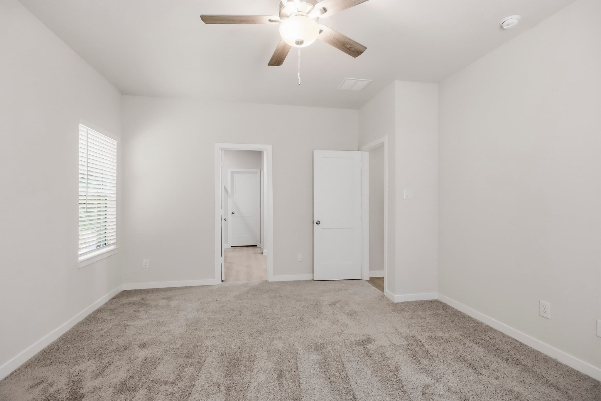 A room with a ceiling fan and white walls.
