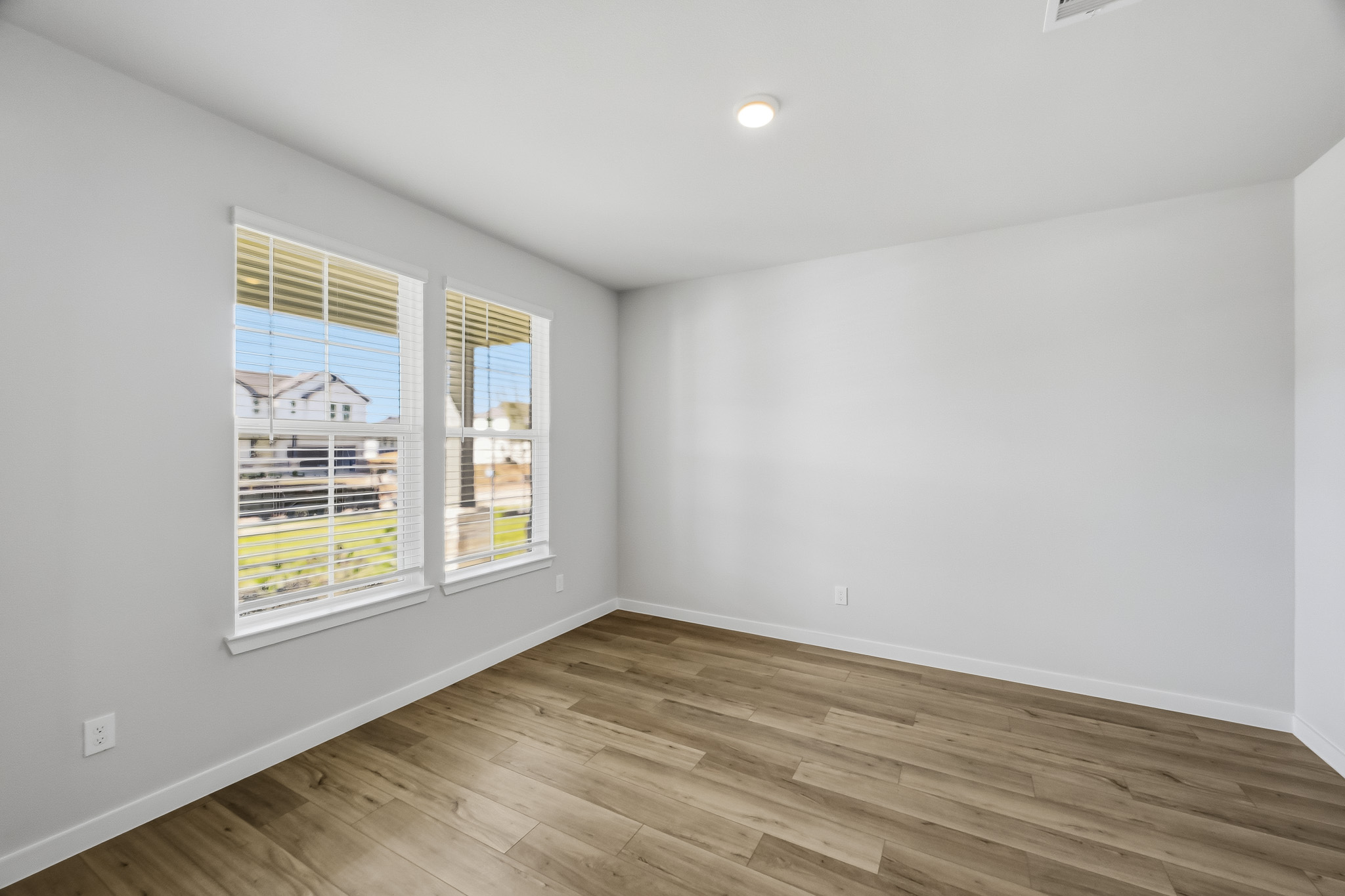 A room with a wood floor and a window with blinds.