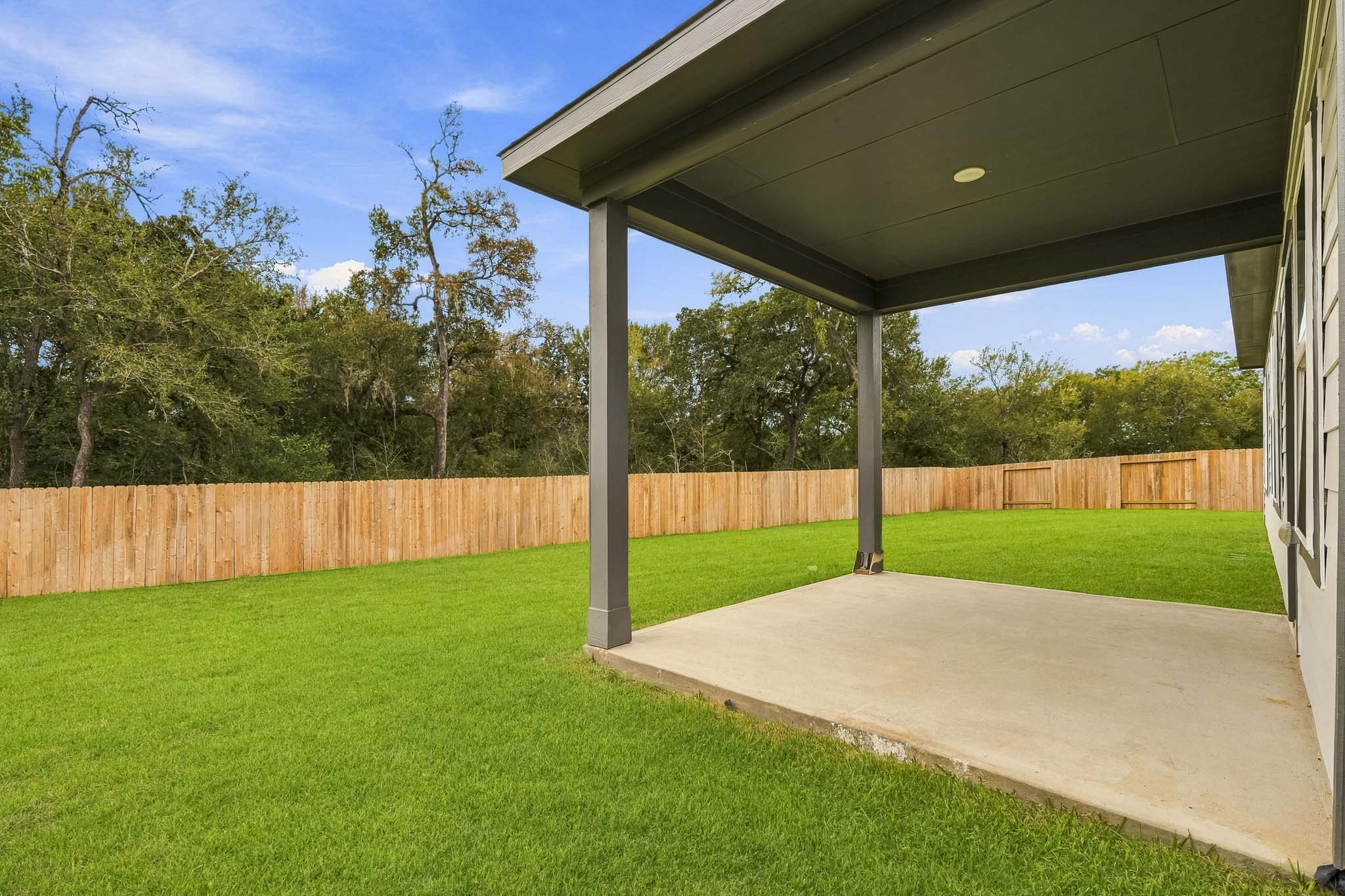 A covered patio with a fence and trees in the background.