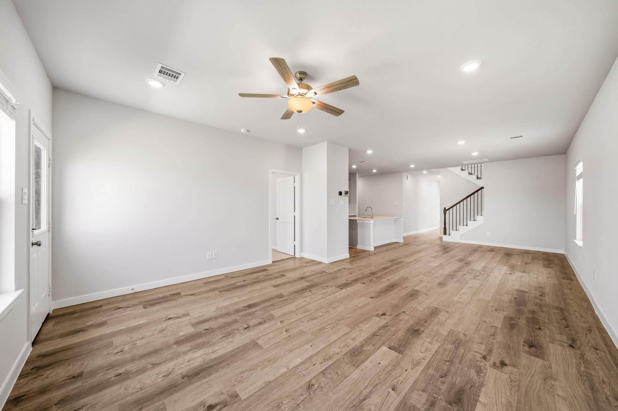 A large empty room with a ceiling fan and wood floors.