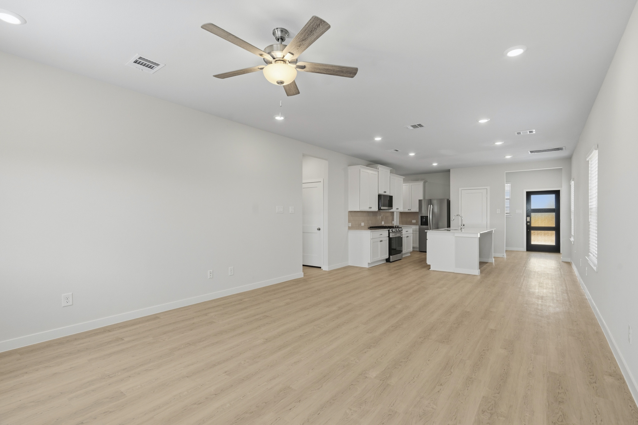 A large empty room with a ceiling fan and a wood floor.