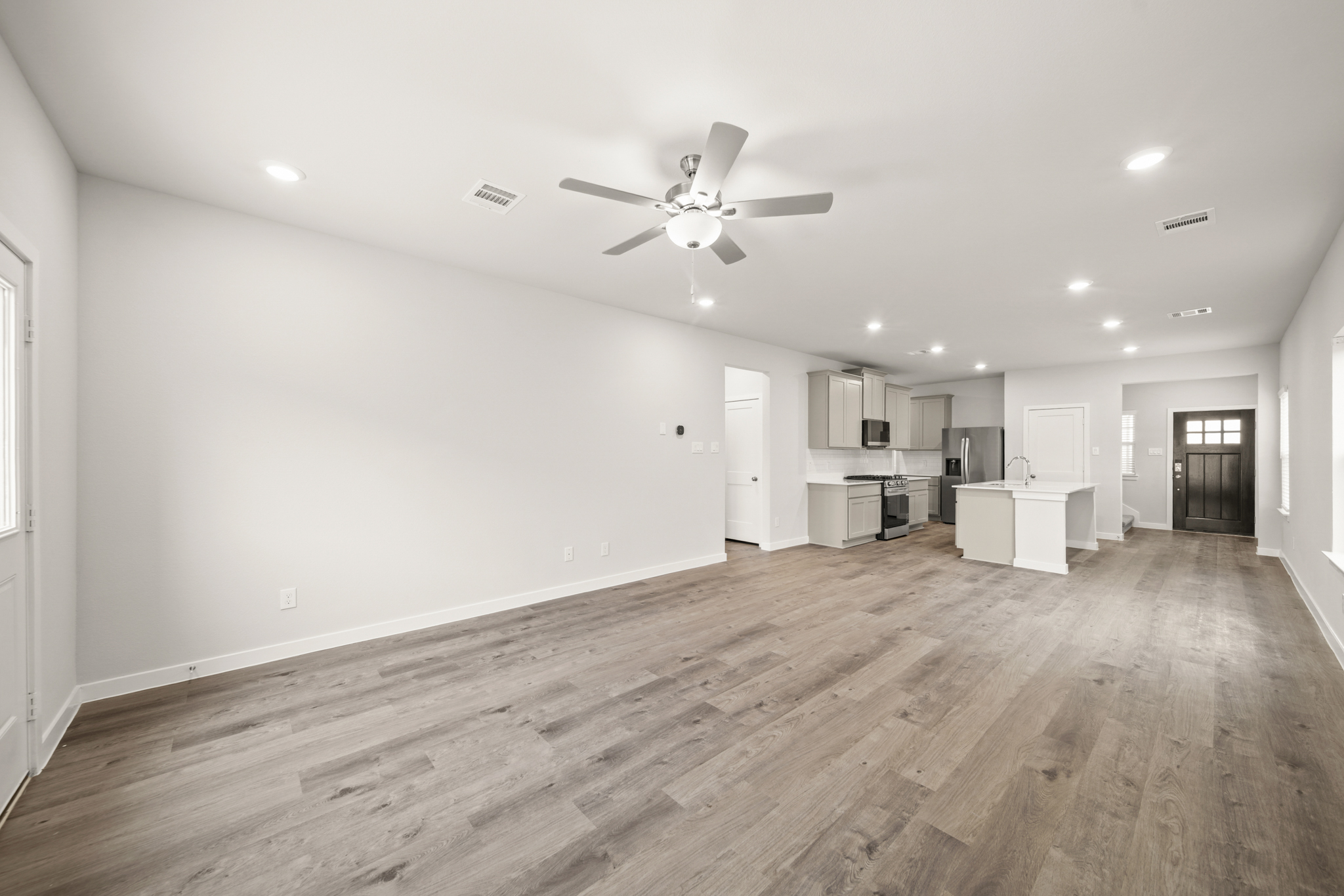 A large empty room with a ceiling fan and a wood floor.