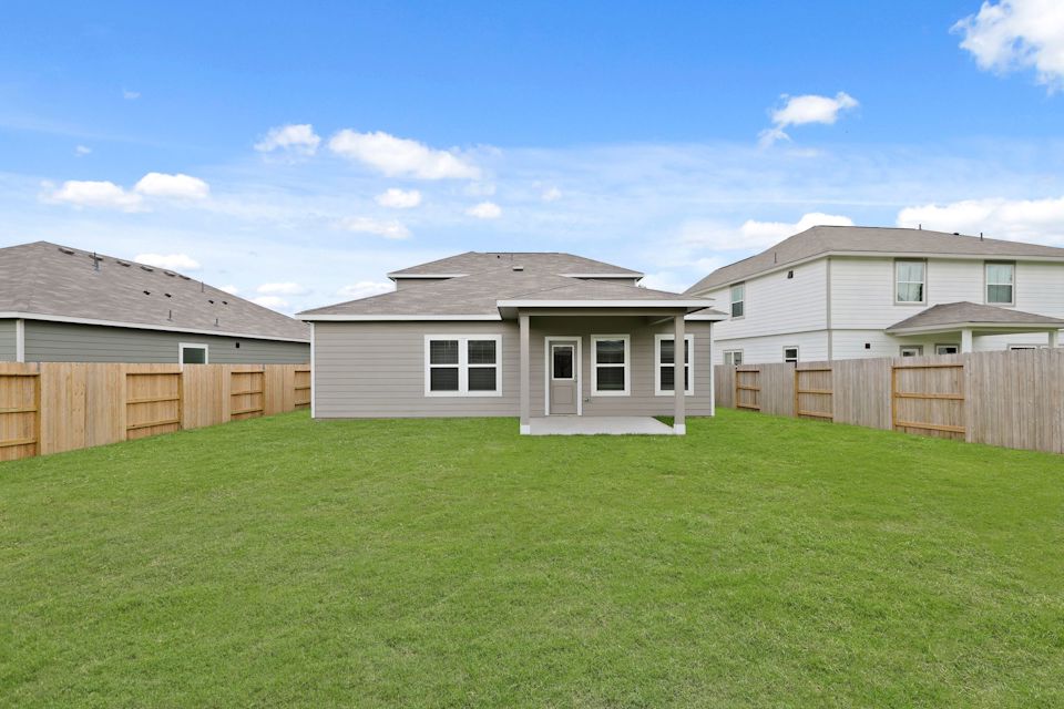 A grassy yard with a fence and houses in the background.