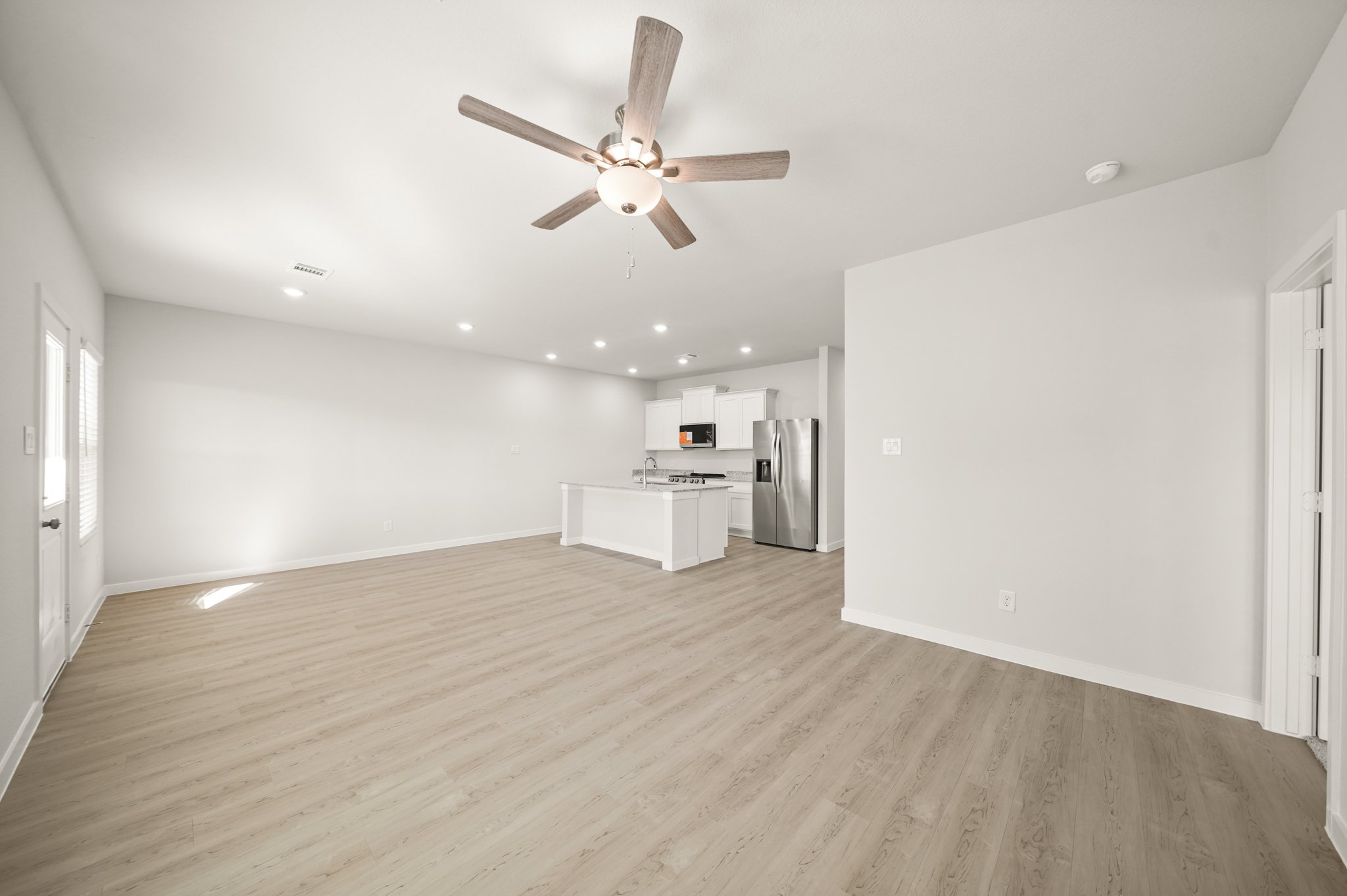 A large empty room with a ceiling fan and a wood floor.