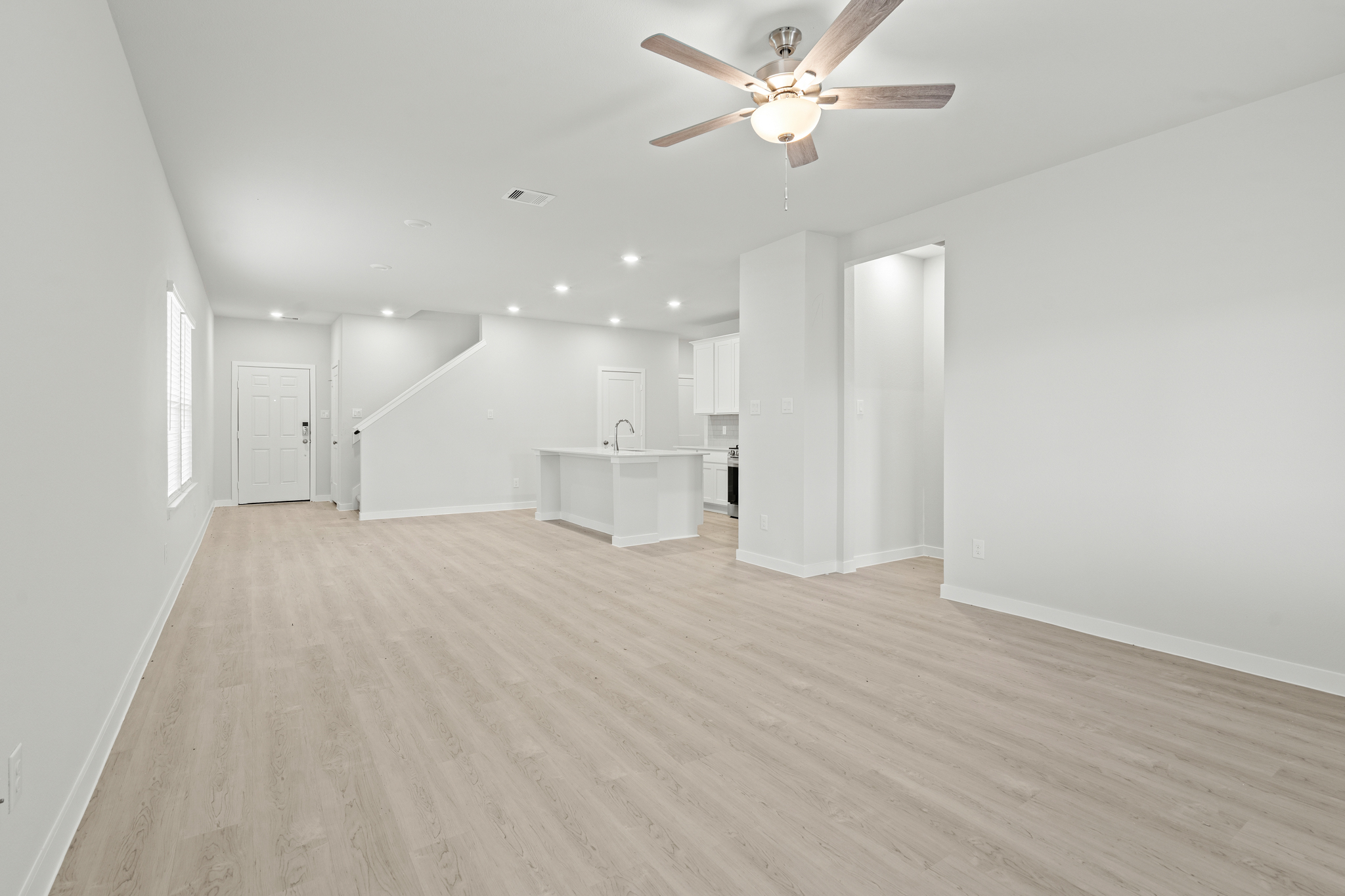 A large empty room with a ceiling fan and white walls.