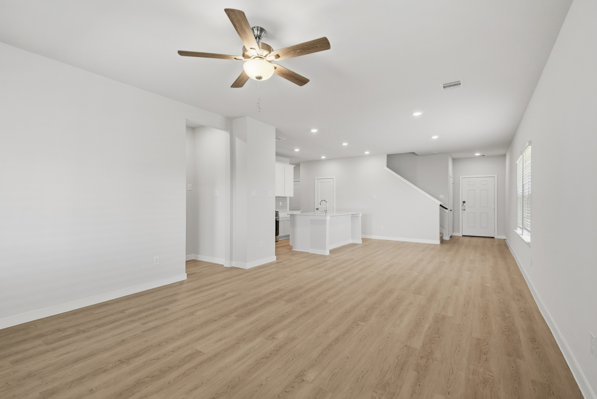 A large empty room with a ceiling fan and a wood floor.
