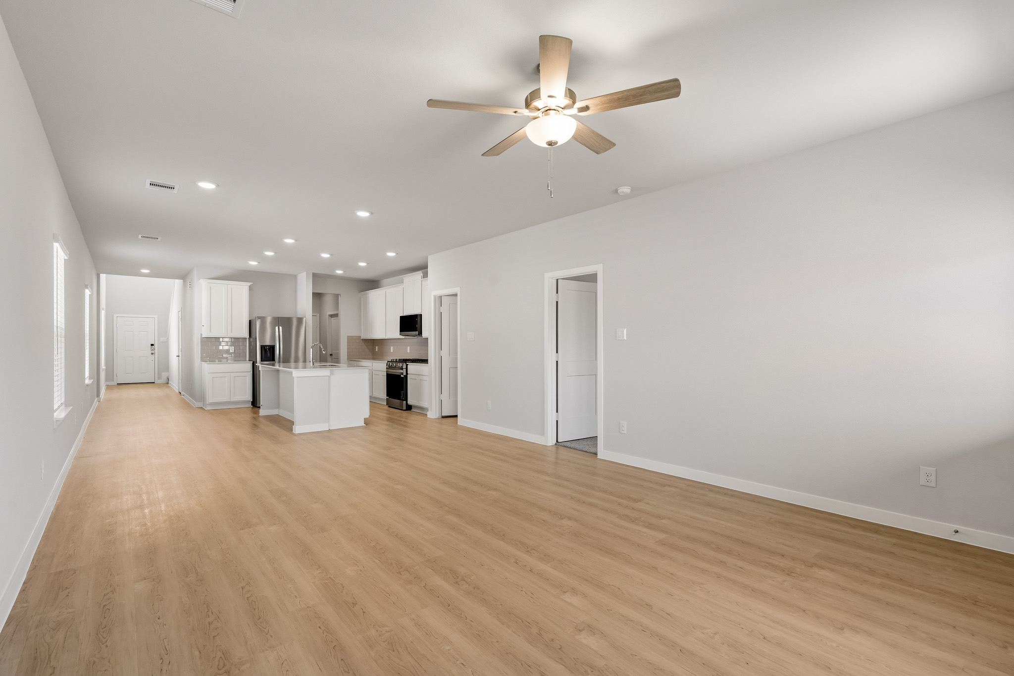 A large empty room with a ceiling fan and a wood floor.