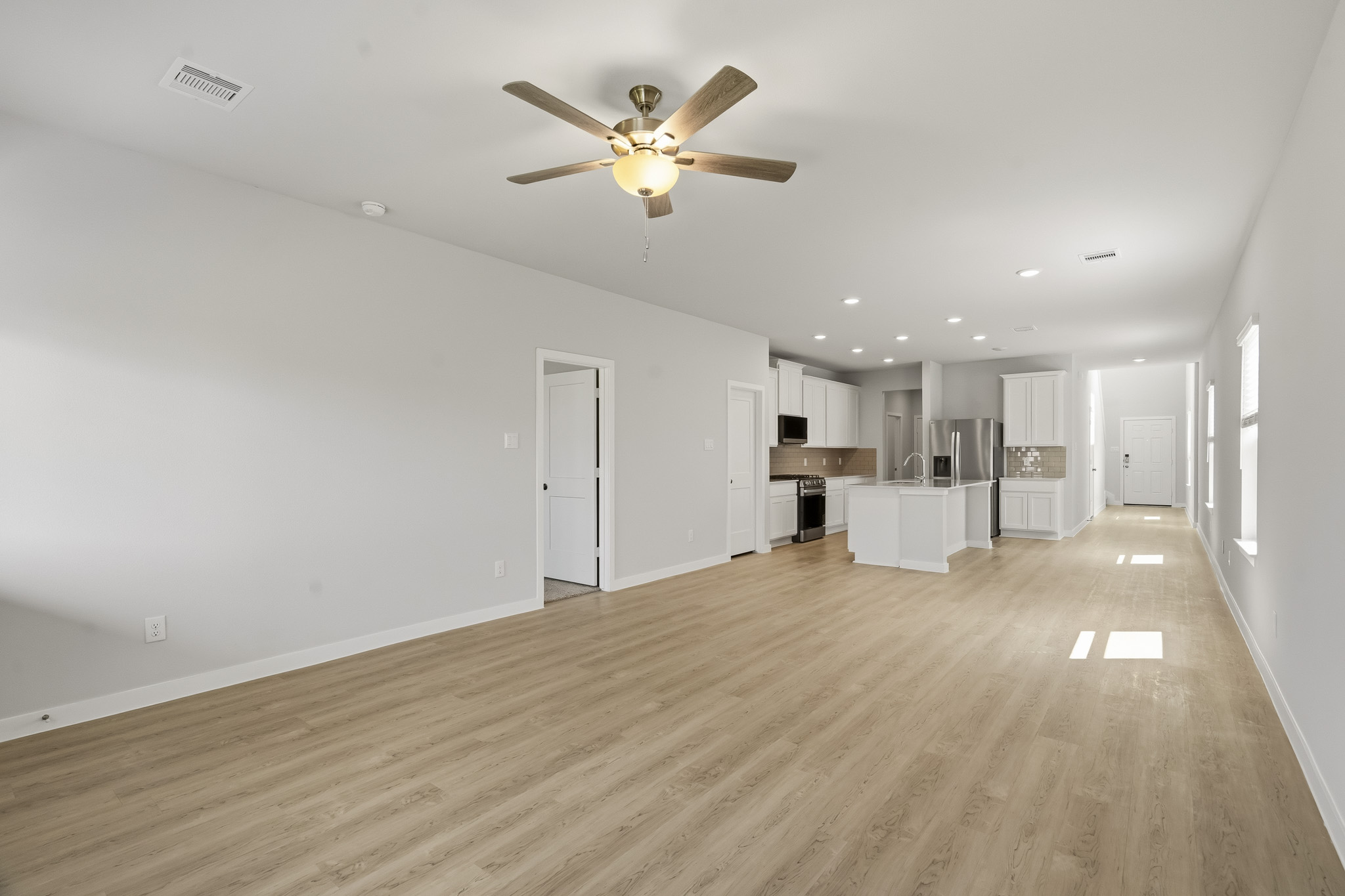 A large empty room with a ceiling fan and a wood floor.