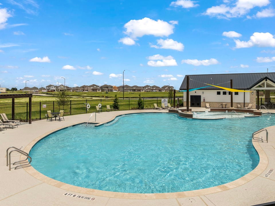 A swimming pool with a fence and buildings in the background.