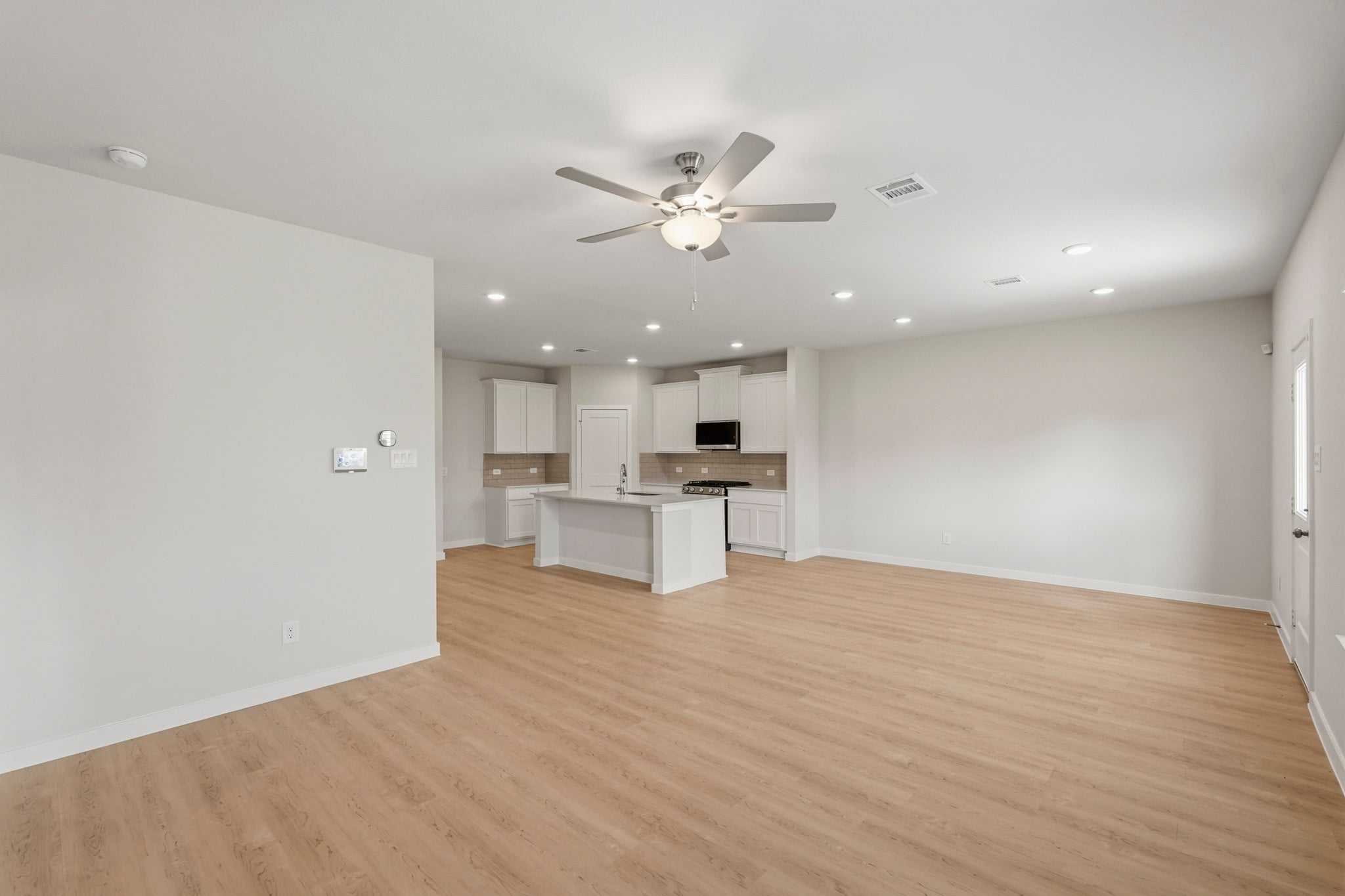 A large empty room with a ceiling fan and a wood floor.