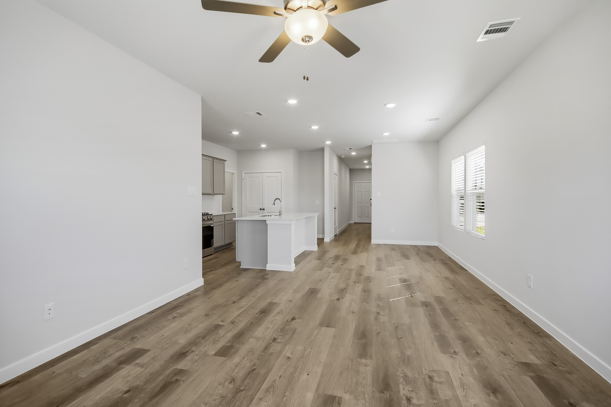 A large empty room with a ceiling fan and a wood floor.