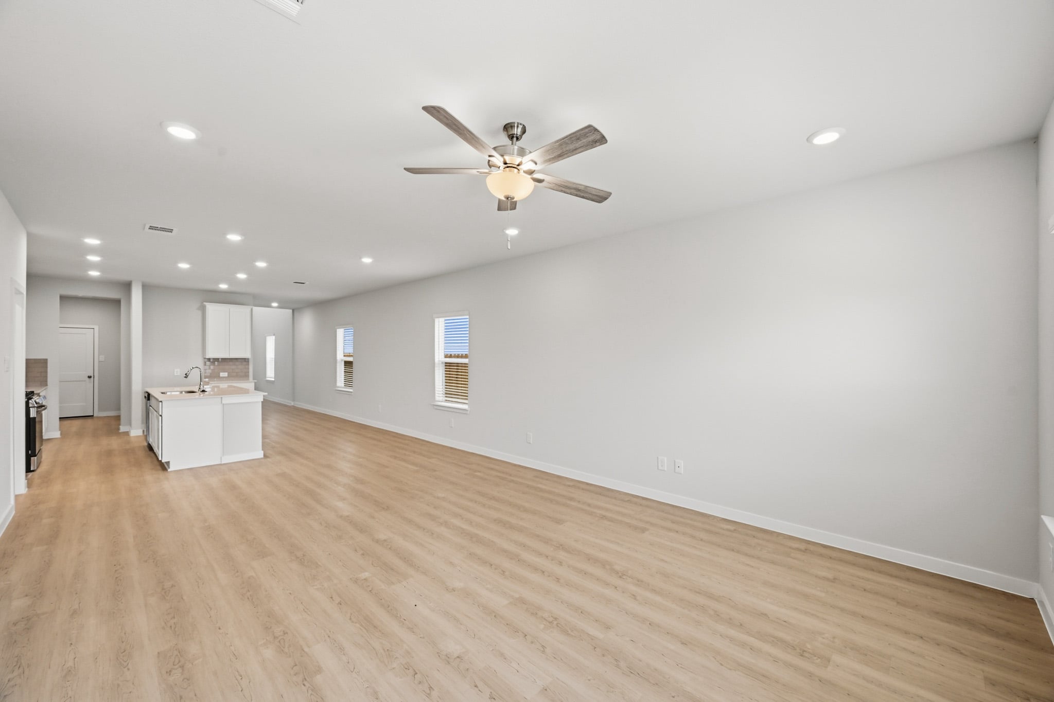 A large empty room with a ceiling fan and a wood floor.