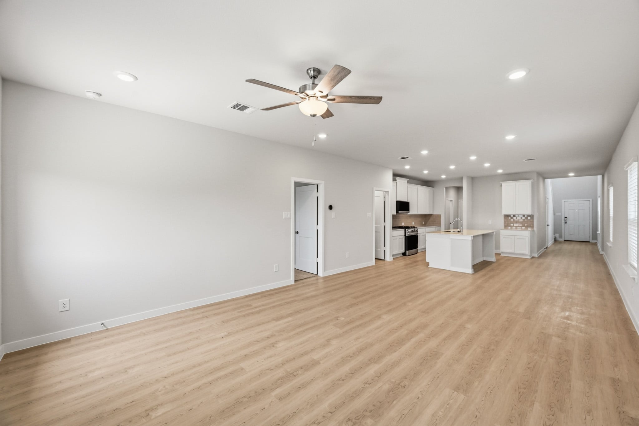 A large empty room with a ceiling fan and a wood floor.