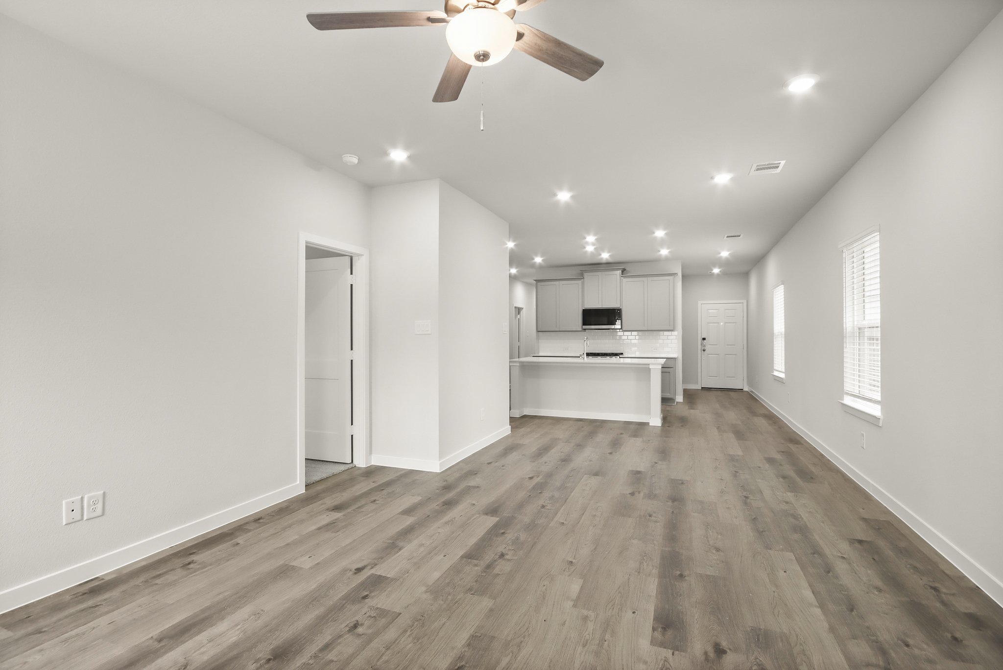 A large empty room with a ceiling fan and a wood floor.