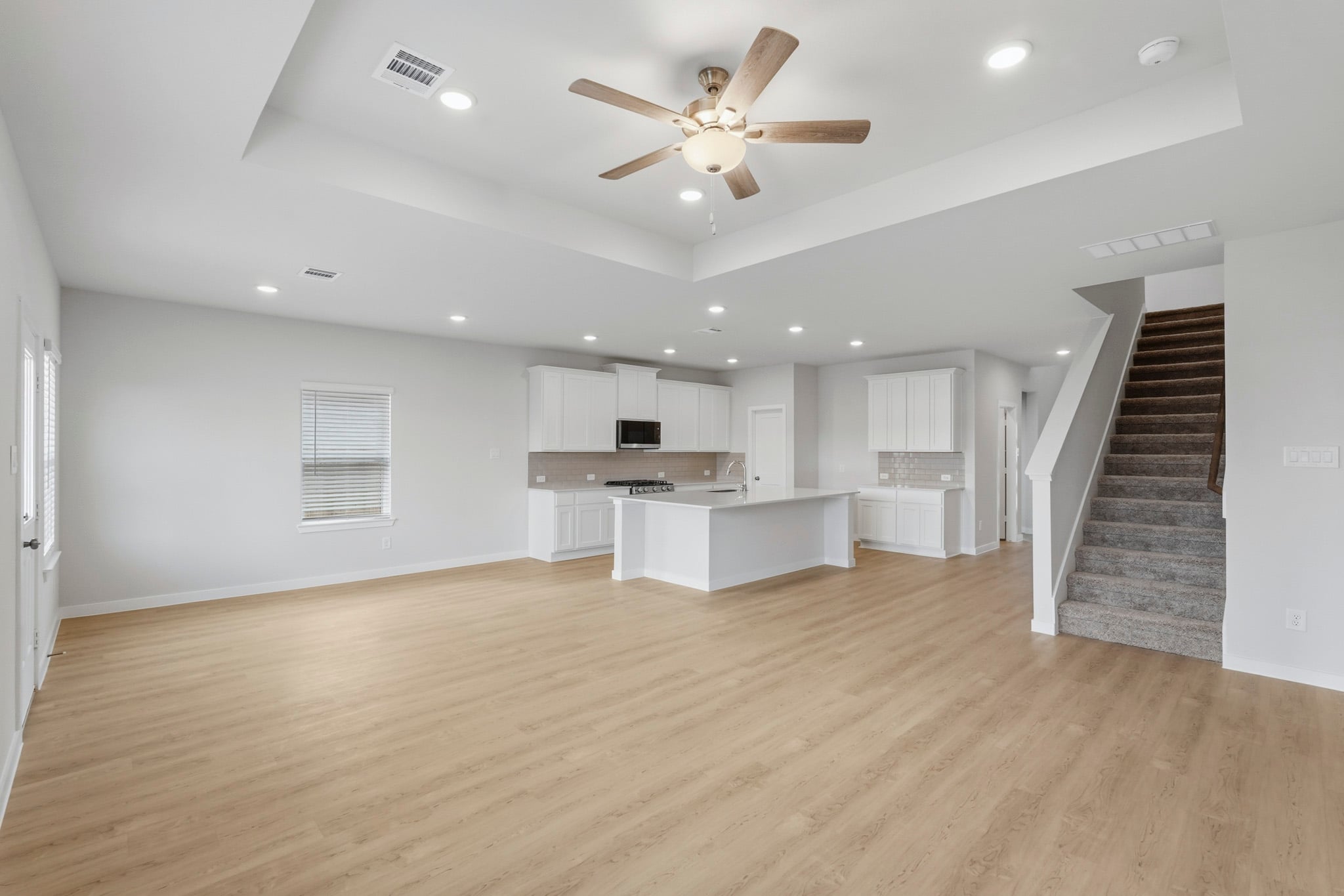 A large empty room with a wood floor and a wood staircase.