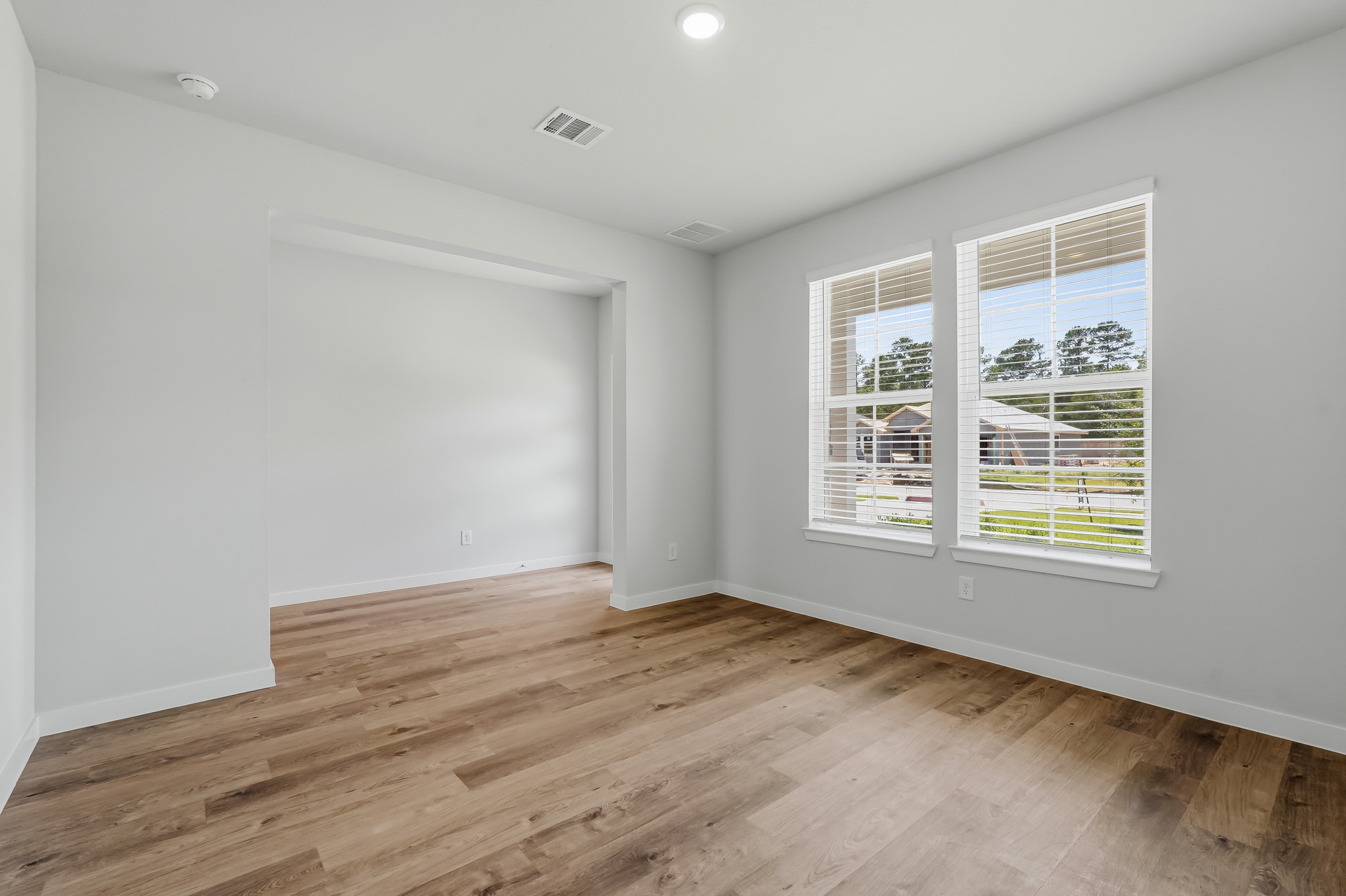 A room with a wood floor and a window with blinds.