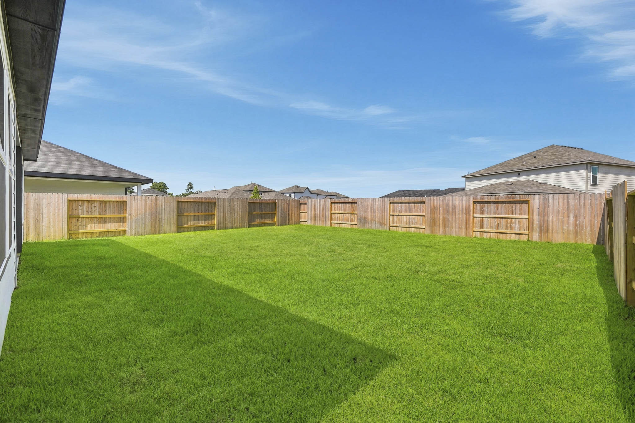 A fenced in yard with a green lawn and a building in the background.