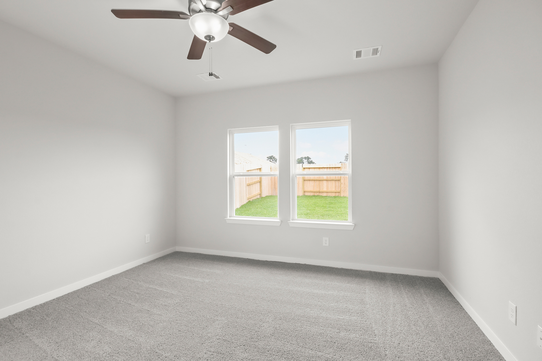 A room with a ceiling fan and a window with a view of the yard.